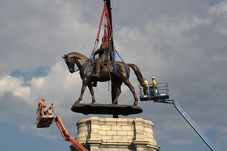 Top of the statue of Lee being hoisted by a crane, with workers in cherry pickers monitoring