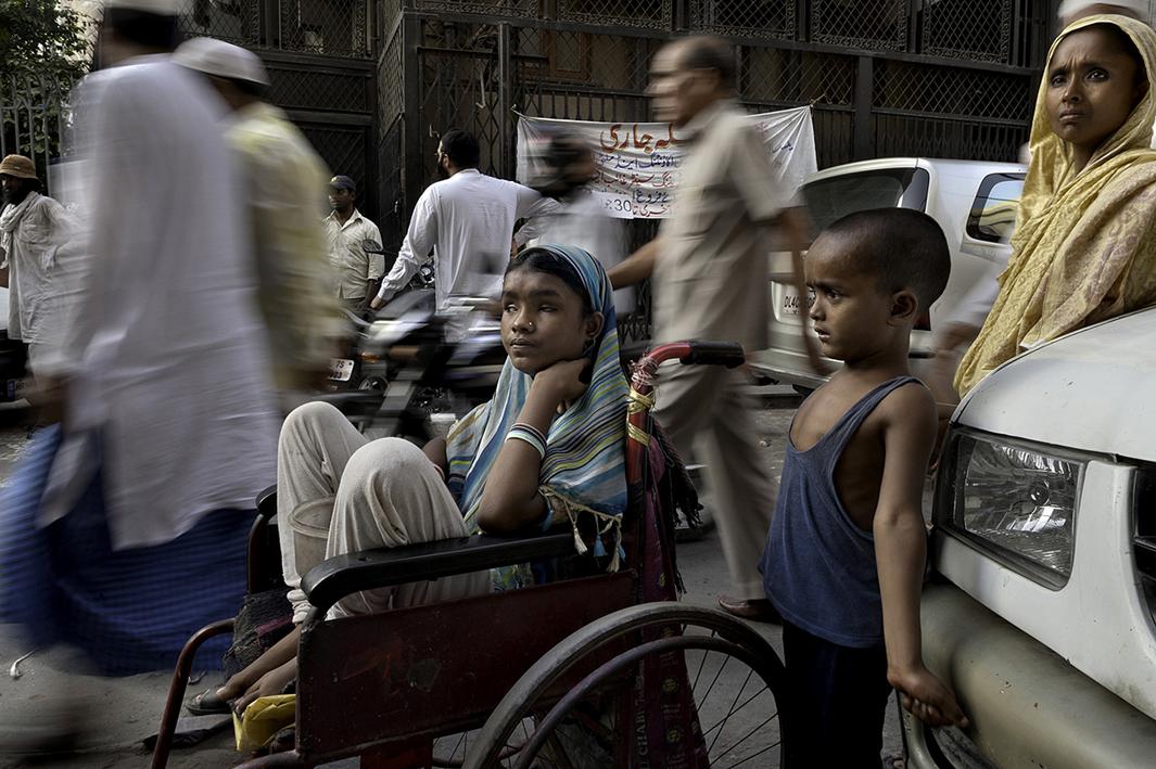 A sea of people passes by Hunupa Begum, 13, who has been blind for the past 10 years and lives close to the Nizamudin Bangala Masjid (Mosque) in New Delhi, India. She begs as the only source of income for her family that consist of a brother Hajimudin Sheikh, 6, center, who suffers fluids that accumulate in his head and her mother Manora Begum, 35, right, who suffers from Asthma, and she has a womb ailment and can't do manual labor. Their father Nizam Ali Sheikh died ten years ago of Tuberculosis. Her wheelchair was donated by a passerby. 