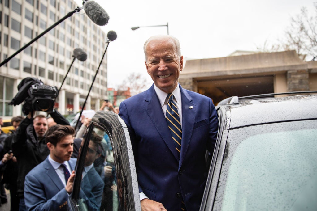 A grinning Biden prepares to get into in to a car as he's followed by reporters.