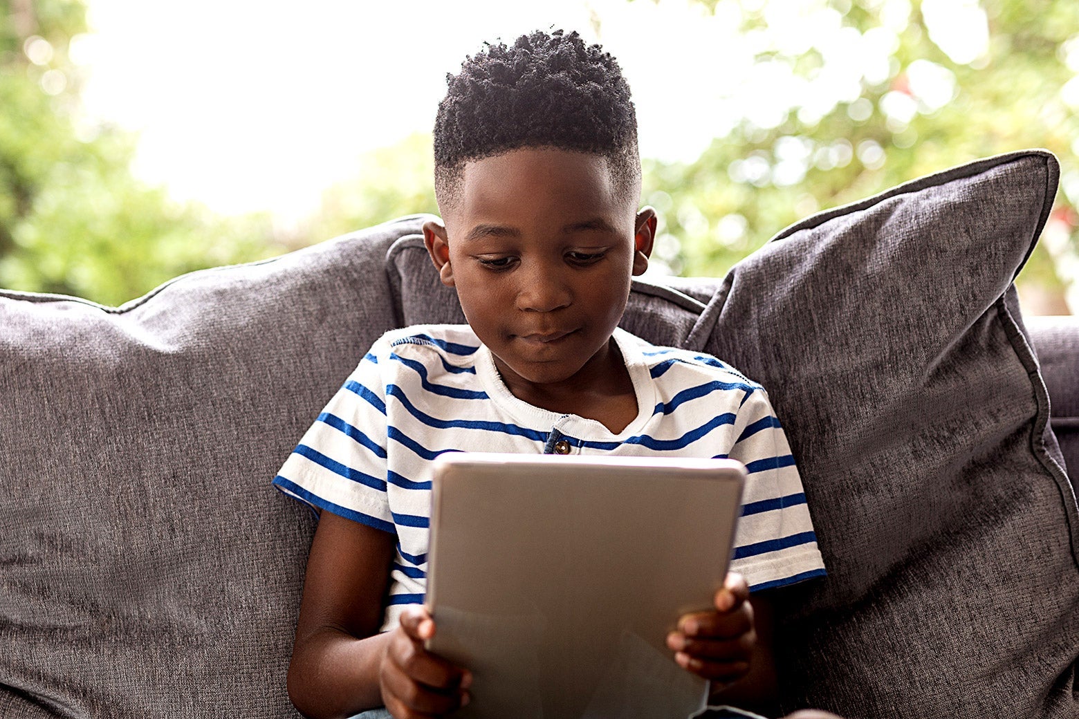 A young Black boy on a couch looking at a tablet.