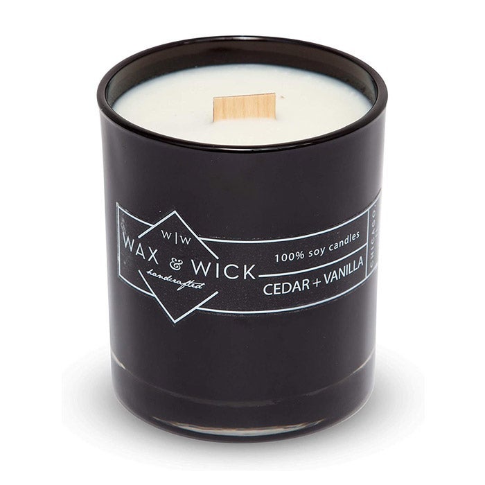 A black jar with a white candle with a wooden wick inside.