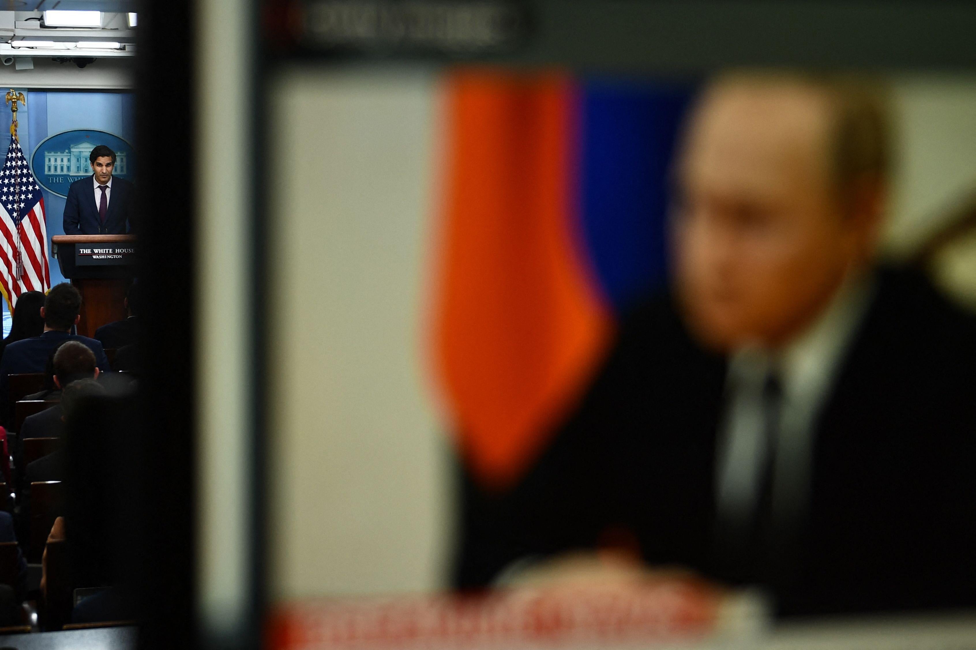 Vladimir Putin pictured on a monitor out of focus in the foreground with deputy national security adviser Daleep Singh speaking at a podium in the White House press briefing room in focus in the background