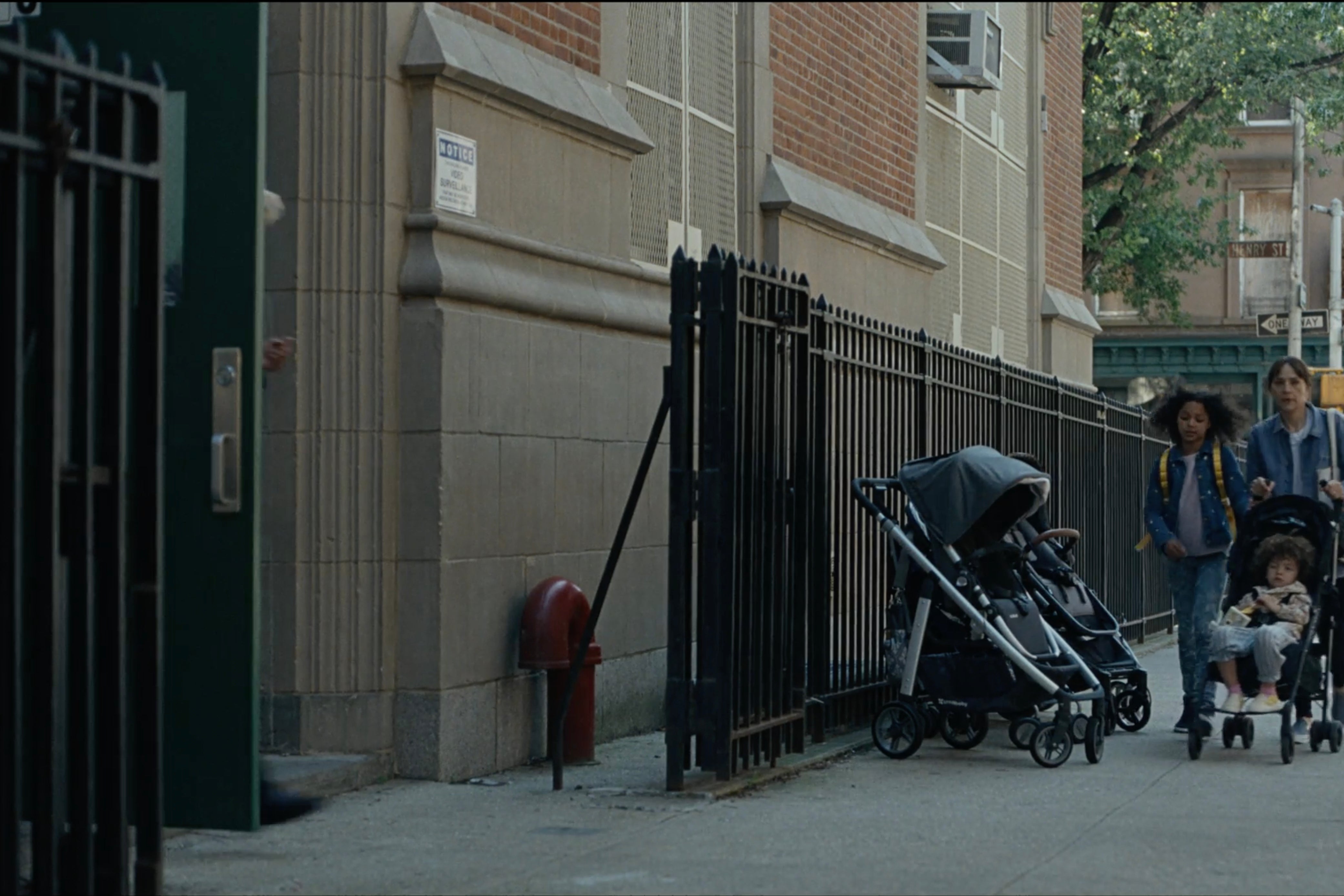 Rashida Jones pushes a stroller with a kid in it and a kid walking beside her down a city street