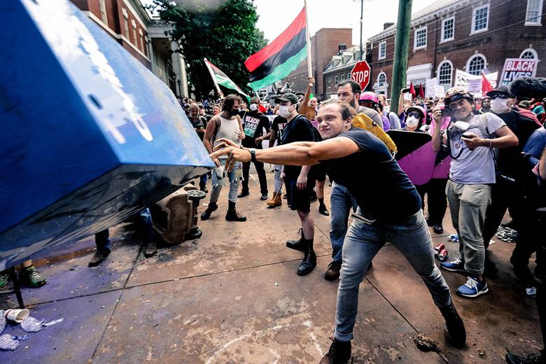 An antifa counterprotester hurls a newspaper box toward Unite the Right rally attendees.