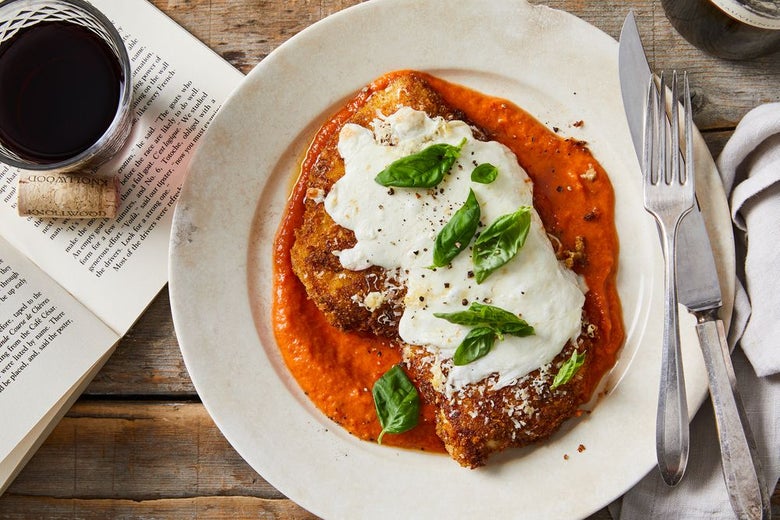 On a plate, a single chicken cutlet in red sauce, topped with white cheese and green leaves.