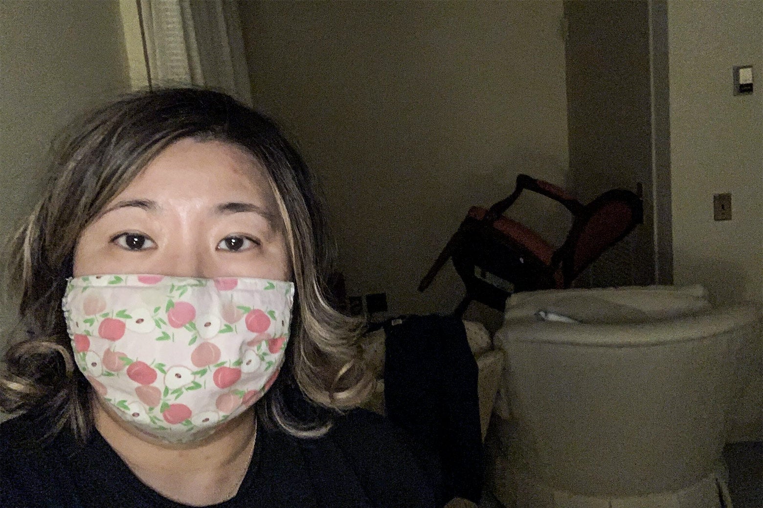 A selfie of Grace Meng in a cloth mask with a chair pushed against a doorknob to barricade the door visible over her shoulder.