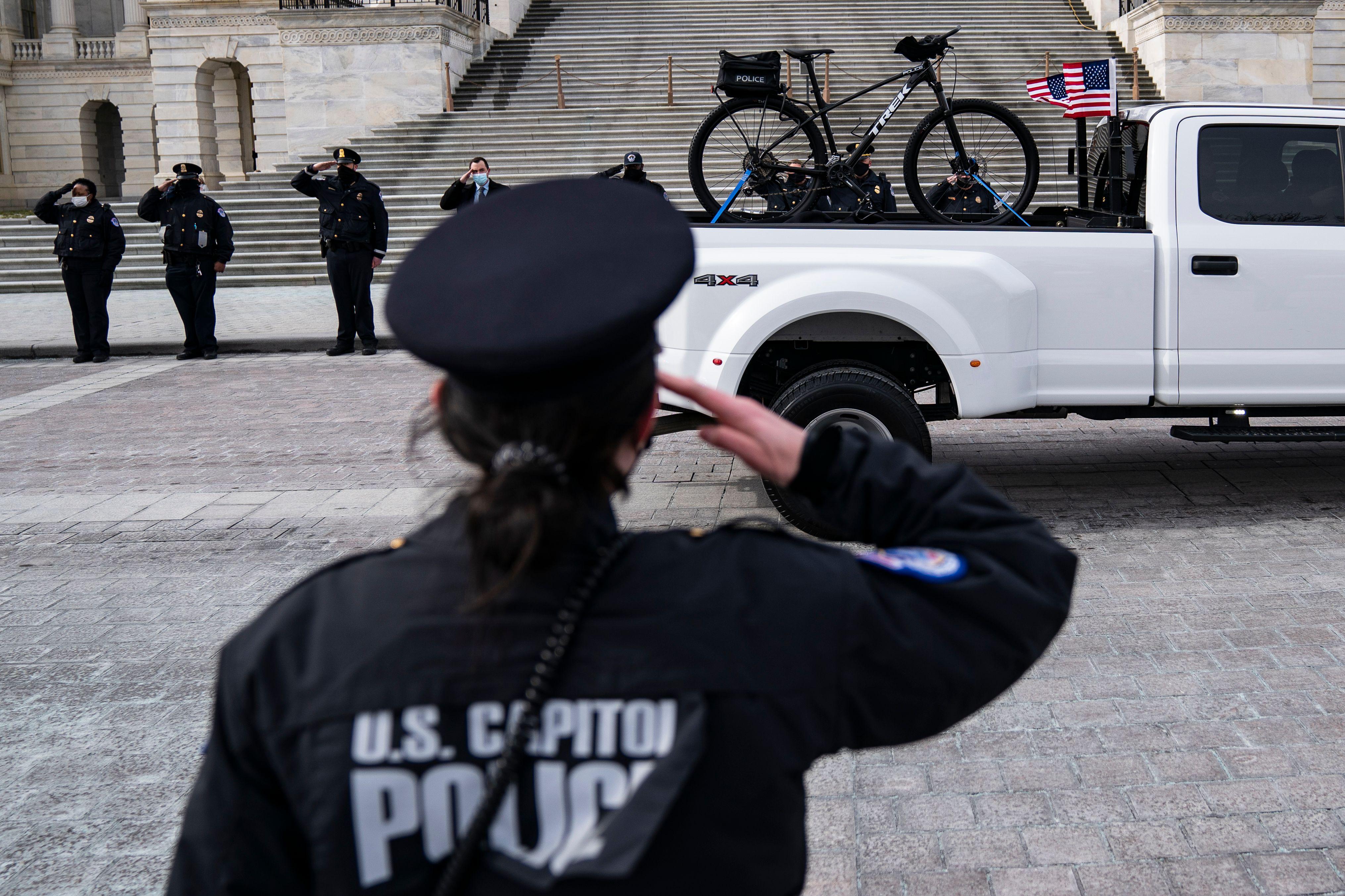 A U.S. Capitol Police office salutes at attention as a truck carrying the bike of US Capitol Police officer Brian Sicknick departs the US Capitol building on February 3, 2021, in Washington, D.C.