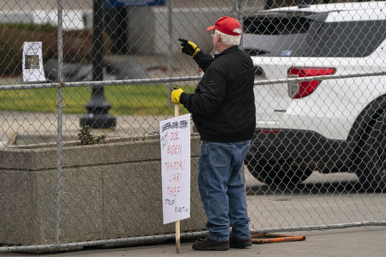 A Trump supporter holding a sign outside a gate.