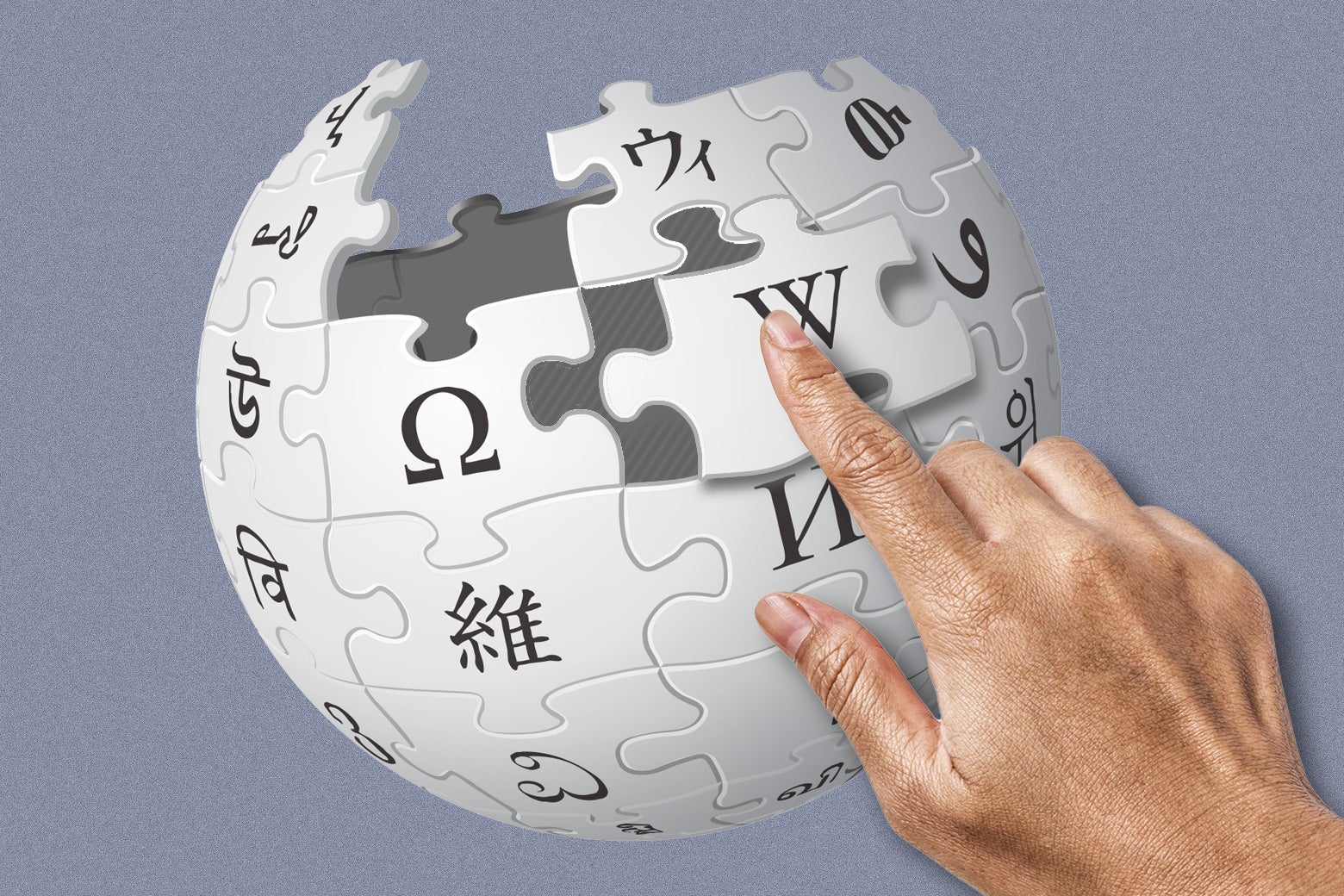 A hand moves a puzzle piece on Wikipedia's logo, a globe made up of puzzle pieces.