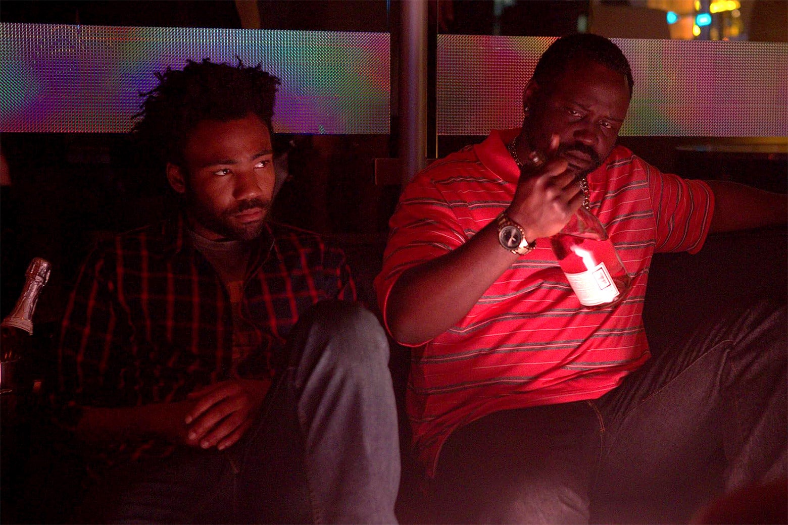 Donald Glover and Brian Tyree Henry sit inside a dimly lit nightclub.