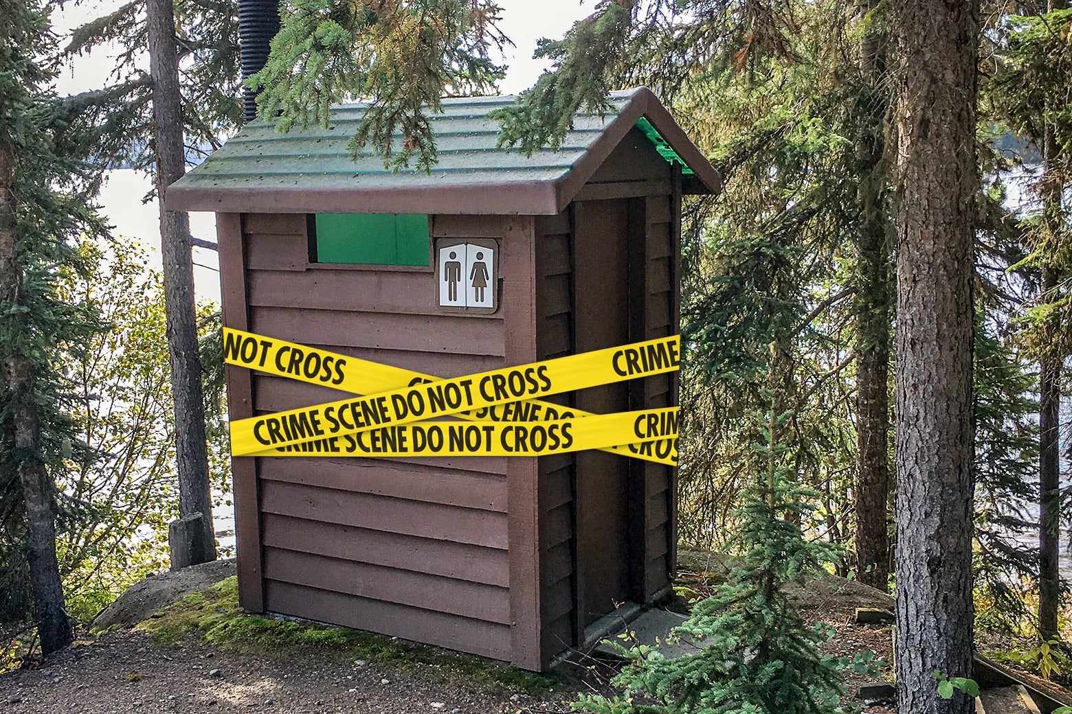Crime scene tape wraps around a public restroom in a wooded area of a park.
