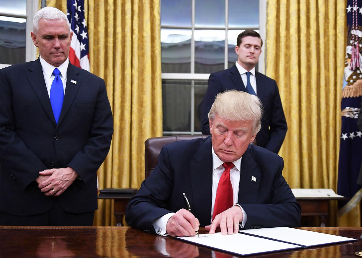 US President Donald Trump signs an executive order as Vice President Mike Pence looks on at the White House in Washington, DC on January 20, 2017.