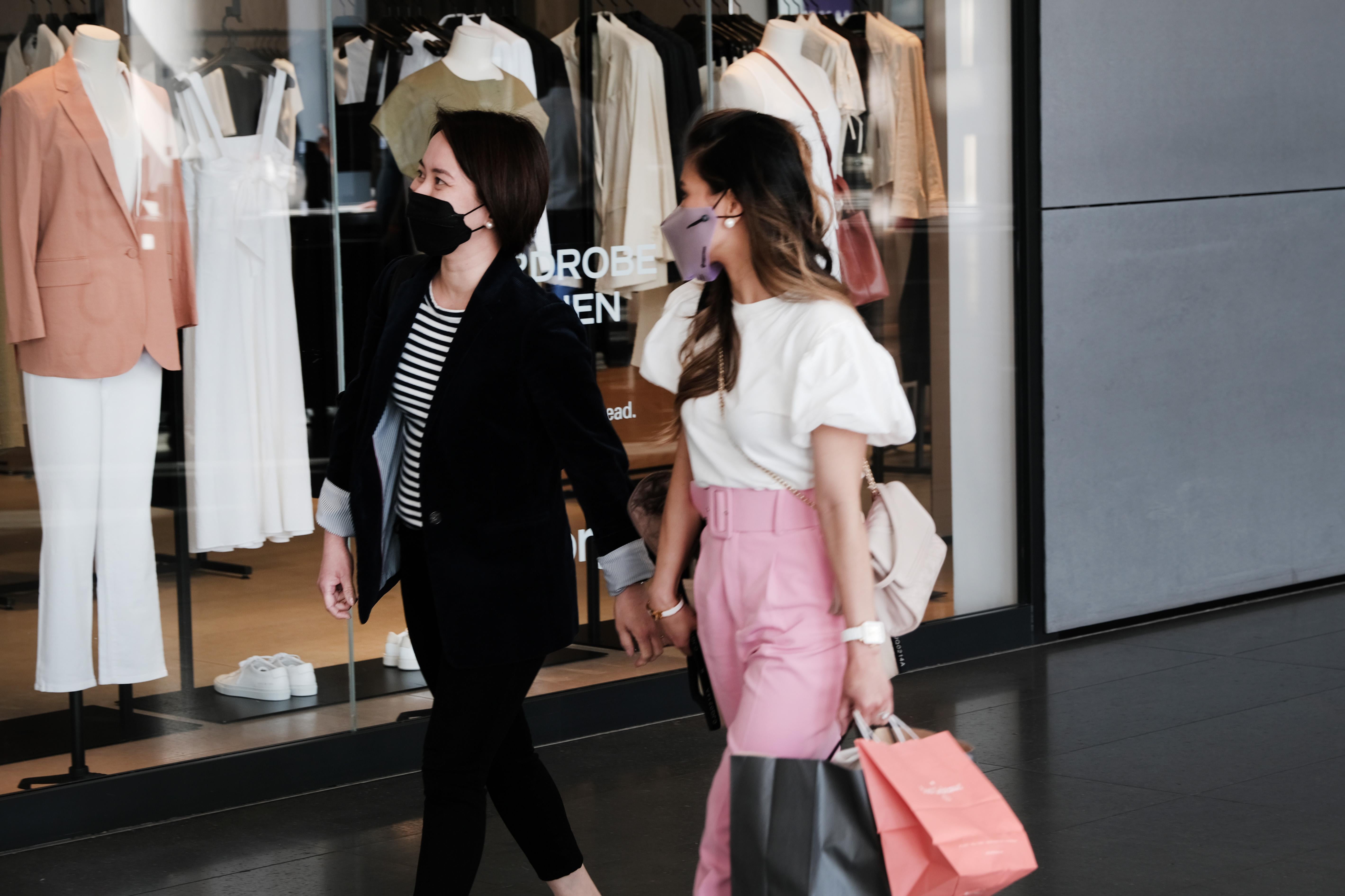 Two women in masks walk through a mall with shopping bags.