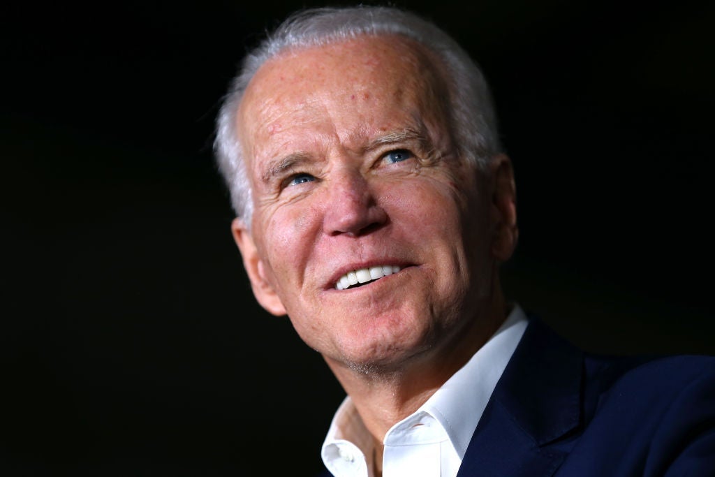 Biden, wearing a blue coat and open-collar white shirt, looks up and to his left against a black backdrop.