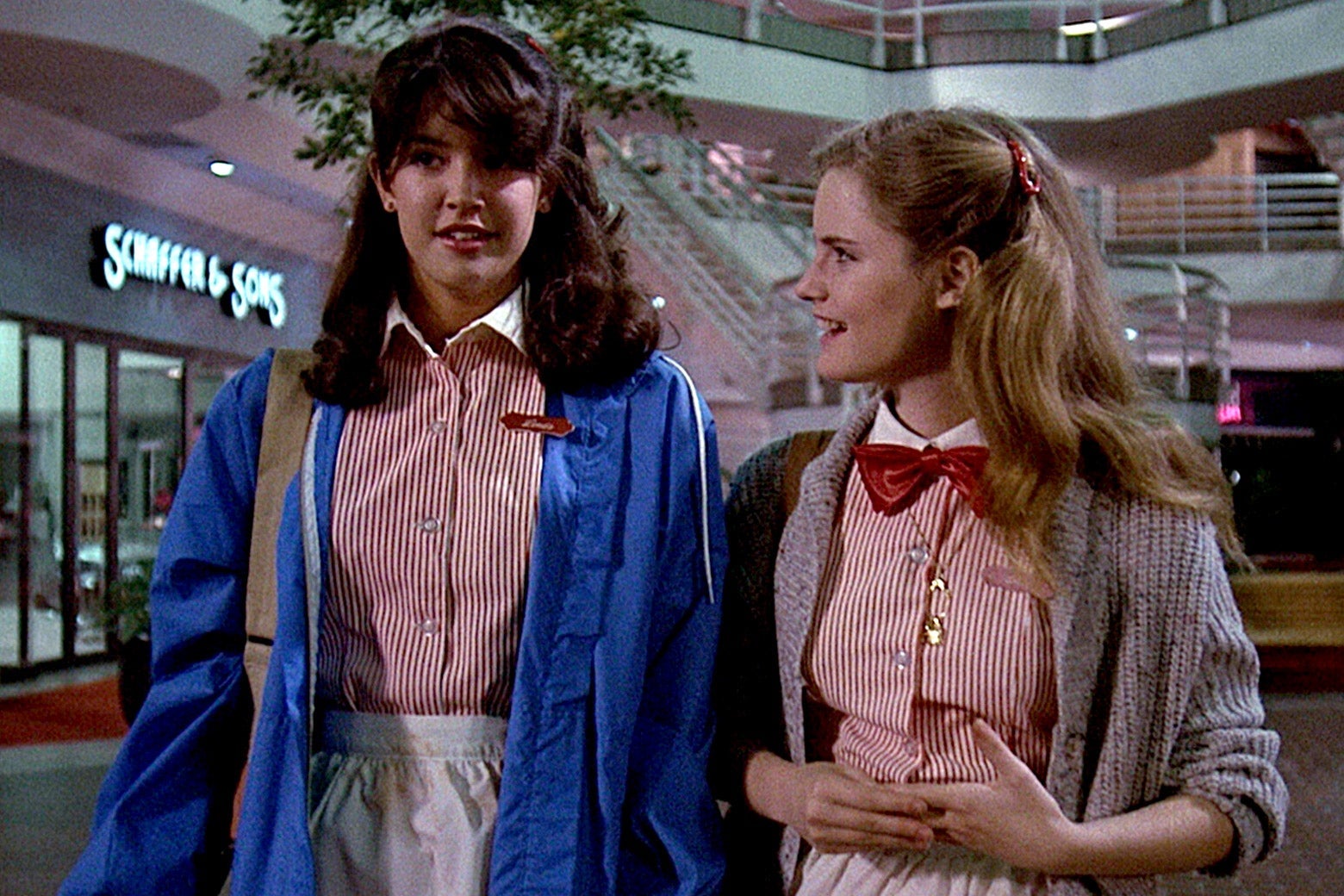 Two teen girls wearing red and white striped restaurant uniforms talking in a mall