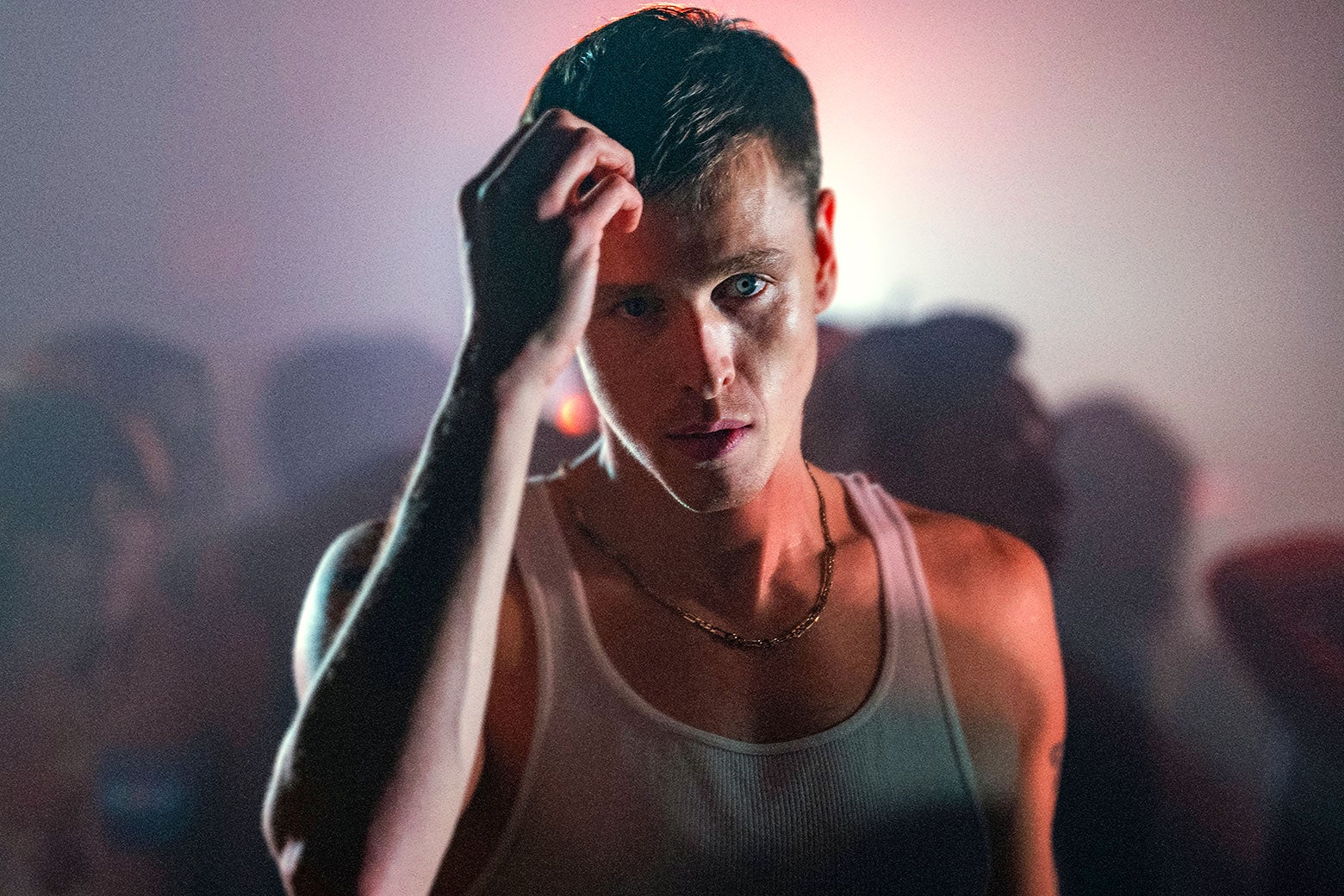 Harris Dickinson in a tank top fixing the front of his hair in a sweaty club.