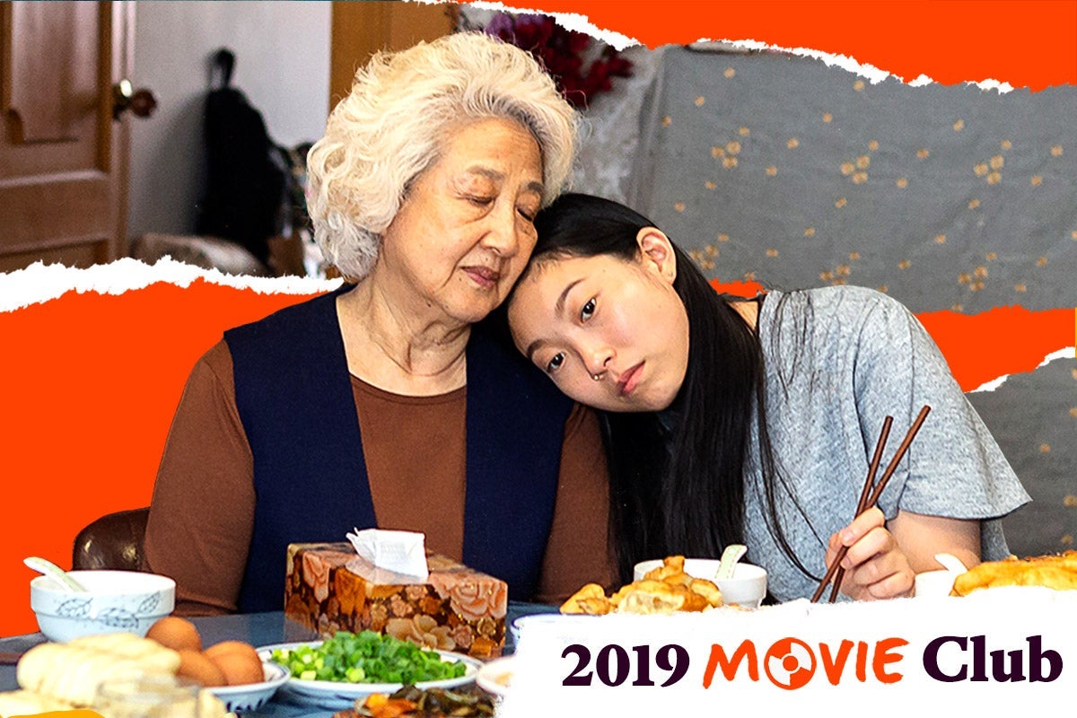 Awkwafina, as Billi, rests her head on the shoulder of Zhao, as Billi's grandmother, as they sit at a table covered in plates of food, in a scene from The Farewell.