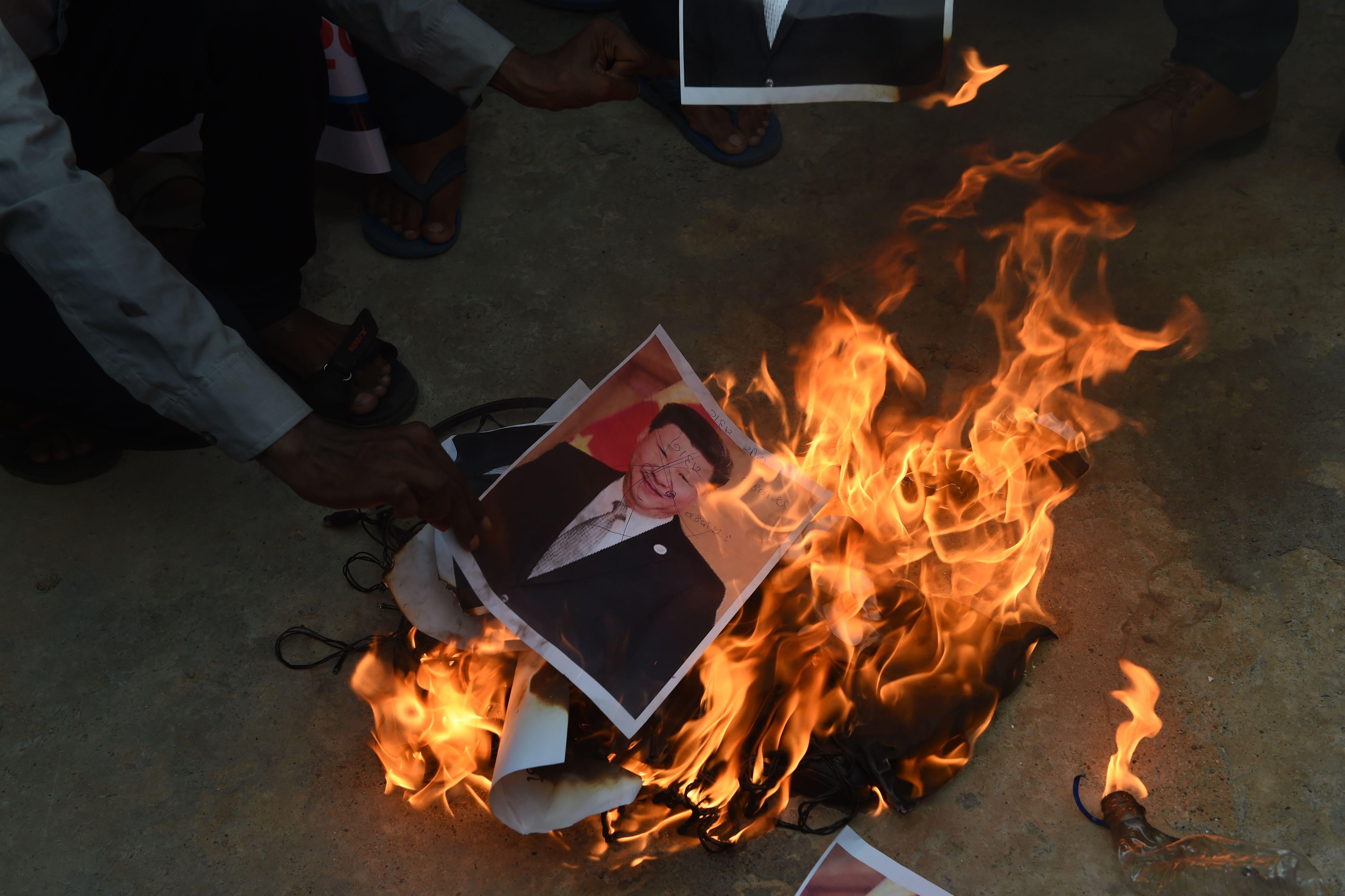 A hand puts photo of Xi Jinping into a ground fire.