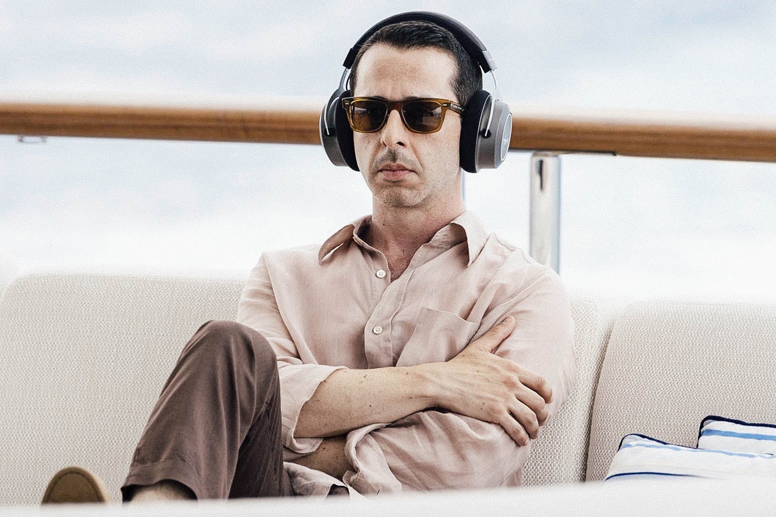 A man crosses his arms against his chest while wearing large headphones and sitting on a yacht.