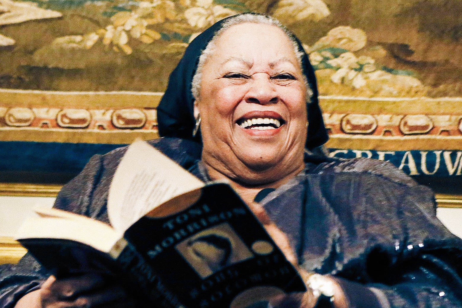Toni Morrison smiling at a reception while turning the page of a book.