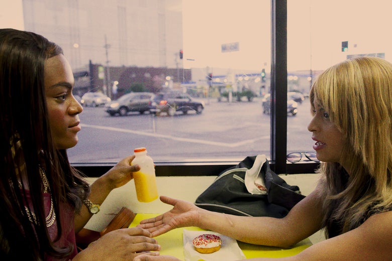 Two transgender women sit at a restaurant table talking to each other over a donut and orange juice.