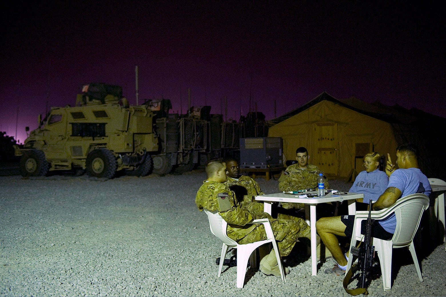 Five people, some in fatigues and some in civilian closes, sit at around a white plastic table in white plastic chairs.