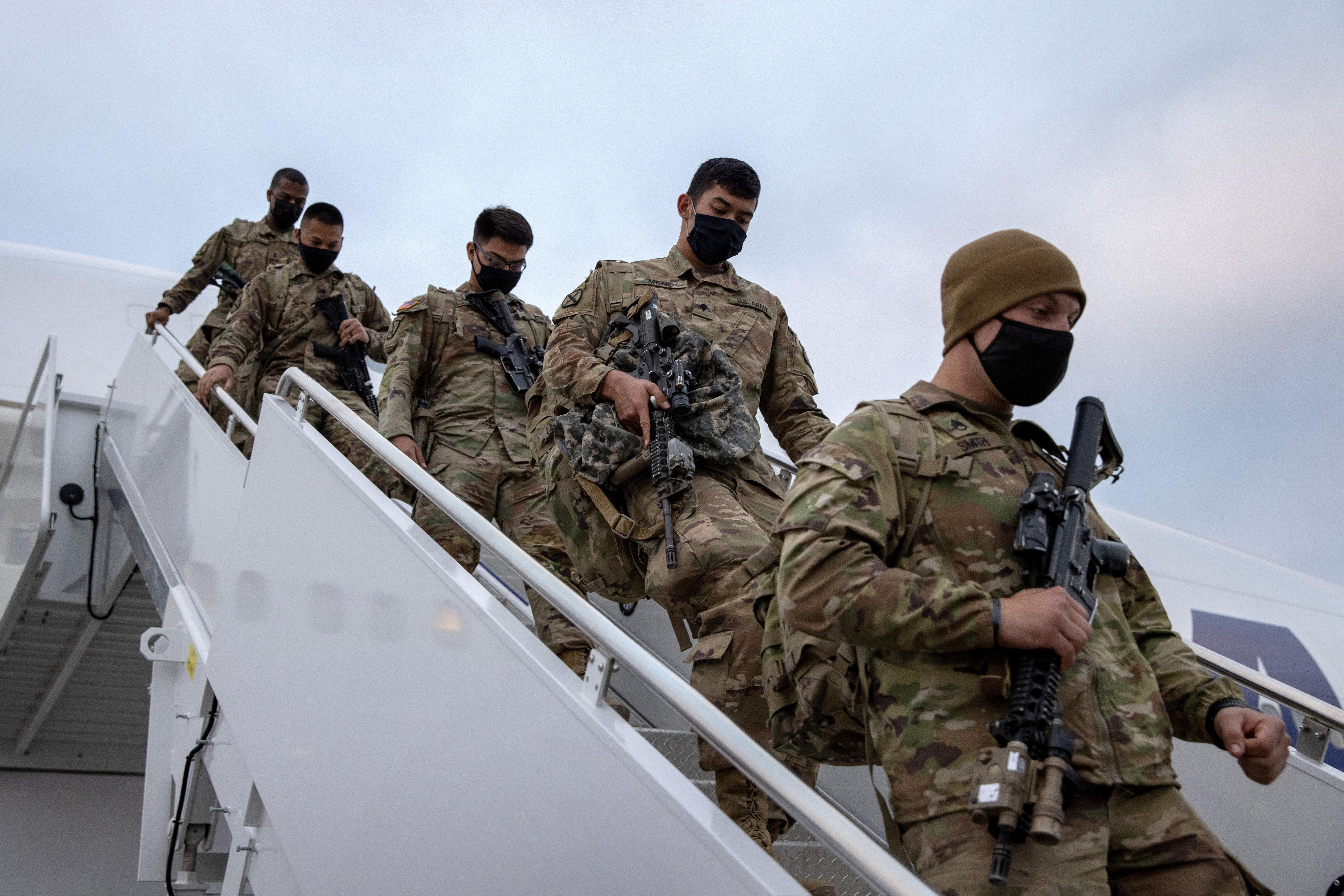 Uniformed troops walking down the stairway from a plane.