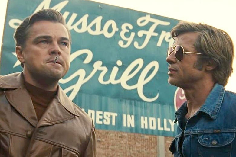 Leonardo DiCaprio and Brad Pitt stand in front of a billboard in a still from the film.