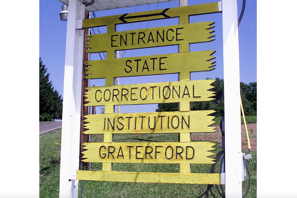A sign that reads: "Entrance State Correctional Institute Grateford in picketed yellow fencing.