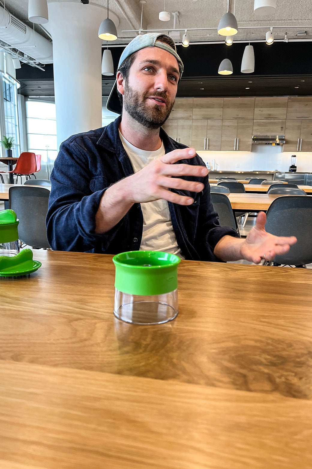 Mack Mor gesticulating while sitting at a table, which holds a small kitchen-appliance piece