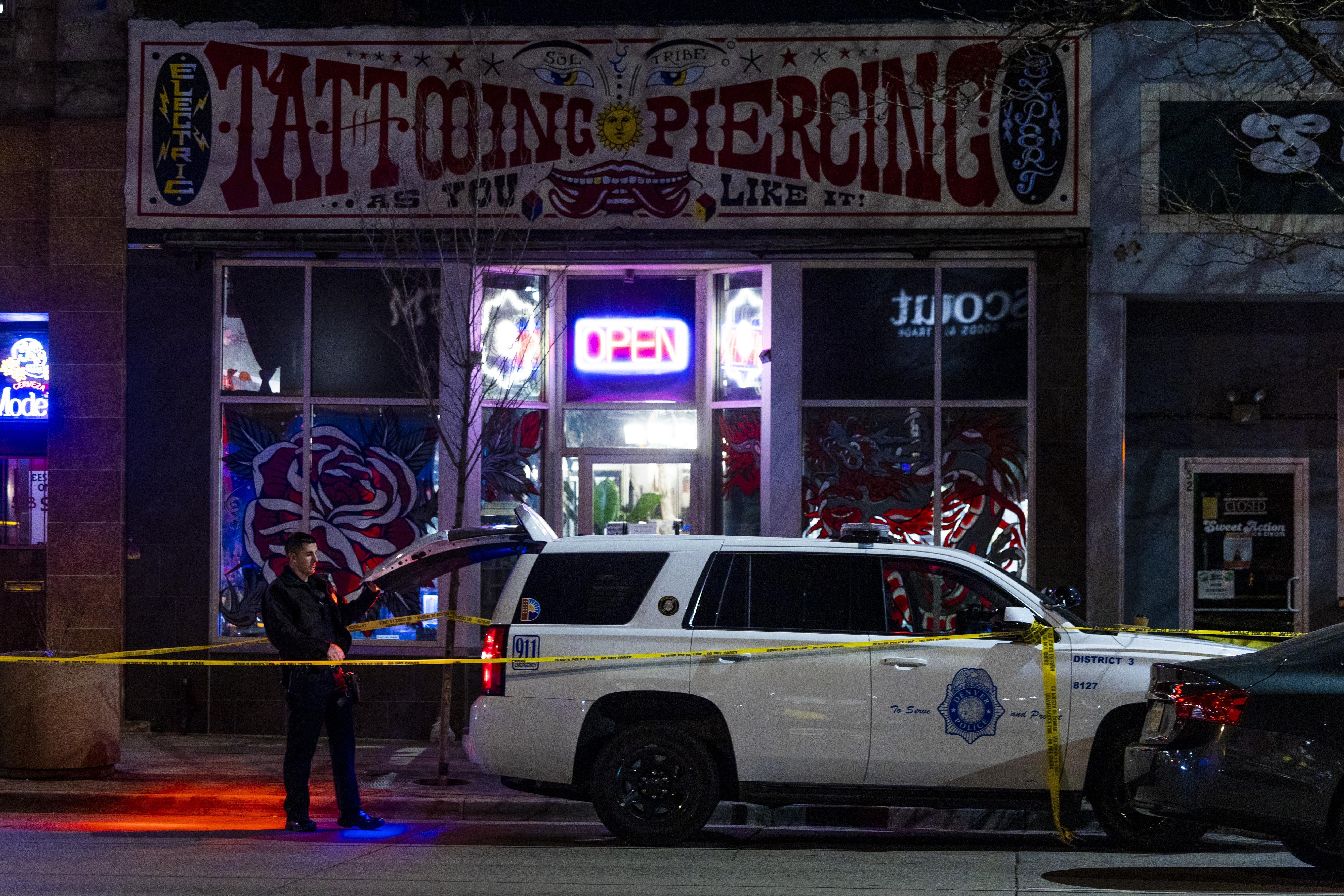 A police car, a police officer, and yellow caution tape in front of a tattoo shop at night