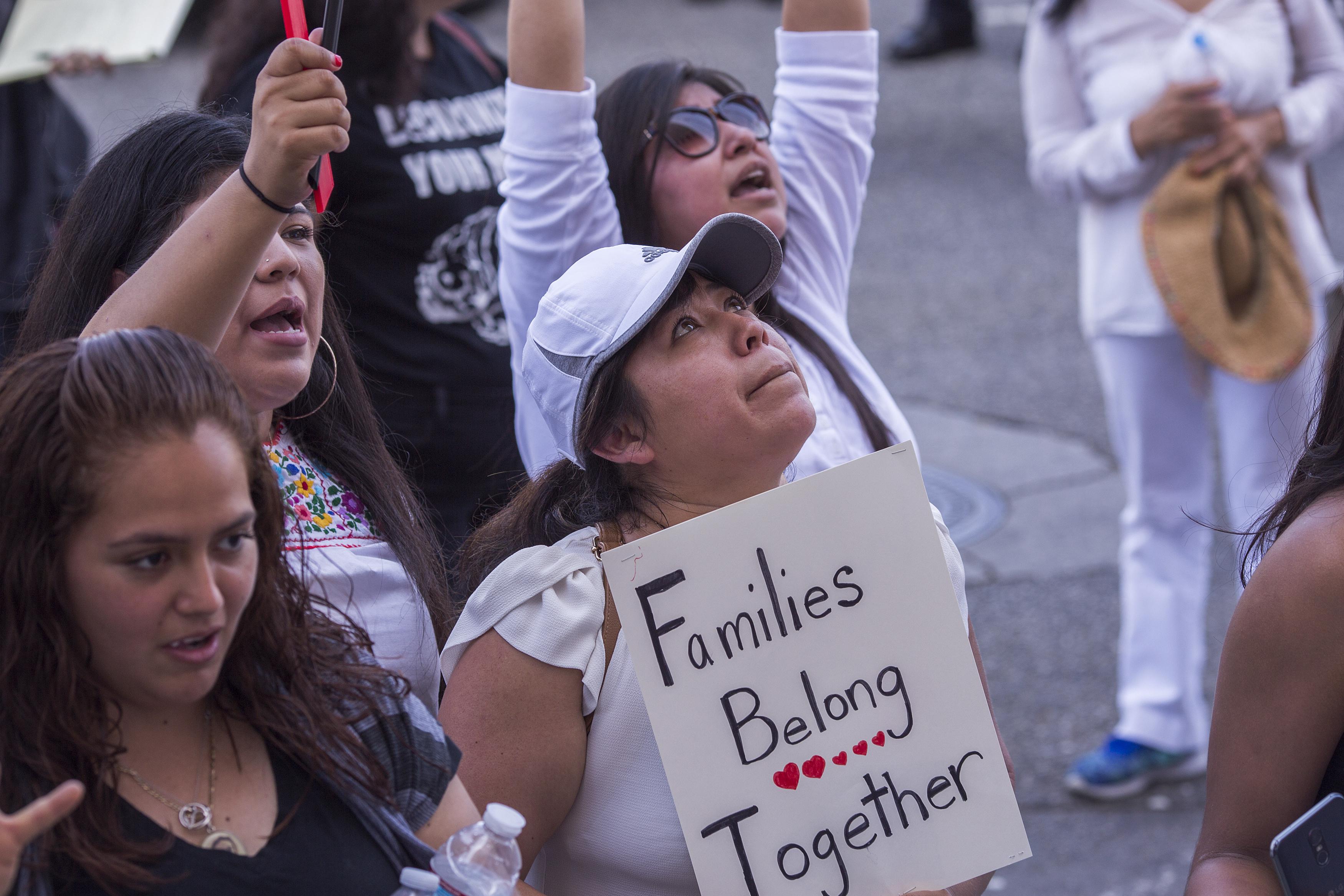 A crying woman holds a sign that reads "Families belong together."