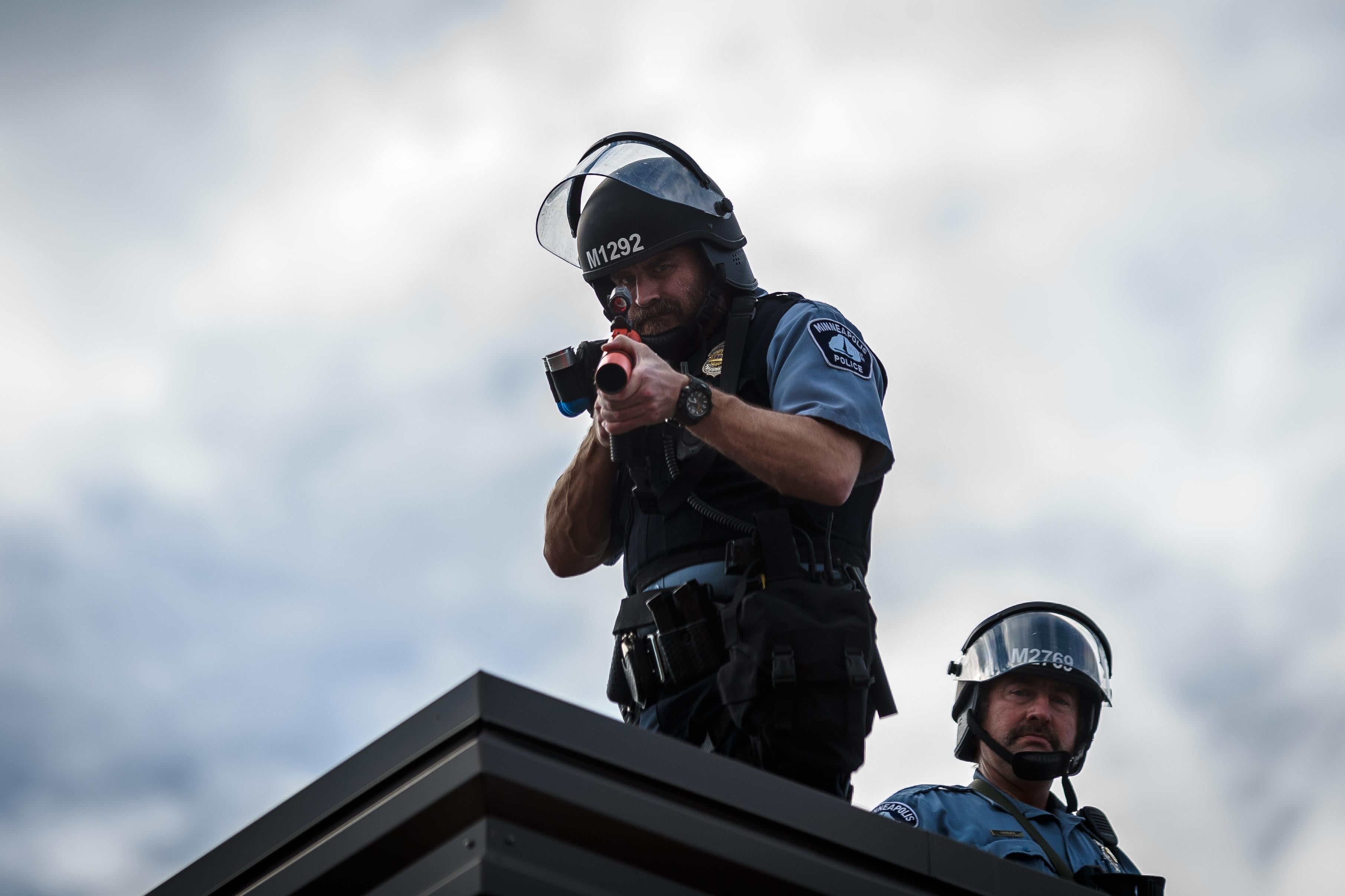 Two police officers stand on the roof, one aiming a weapon toward the camera.