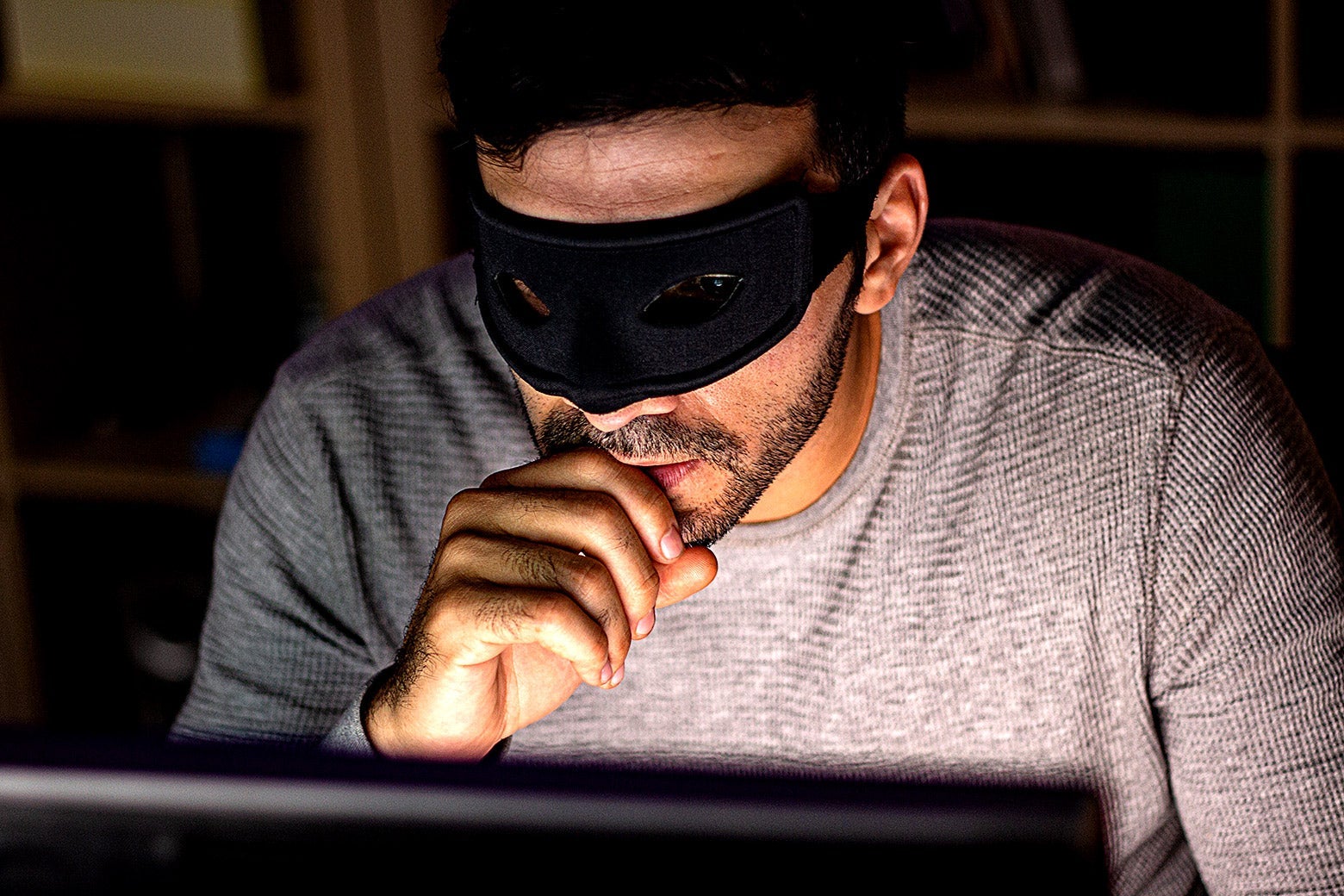 A man in an eye mask looks at a laptop screen with his hand on his mouth.