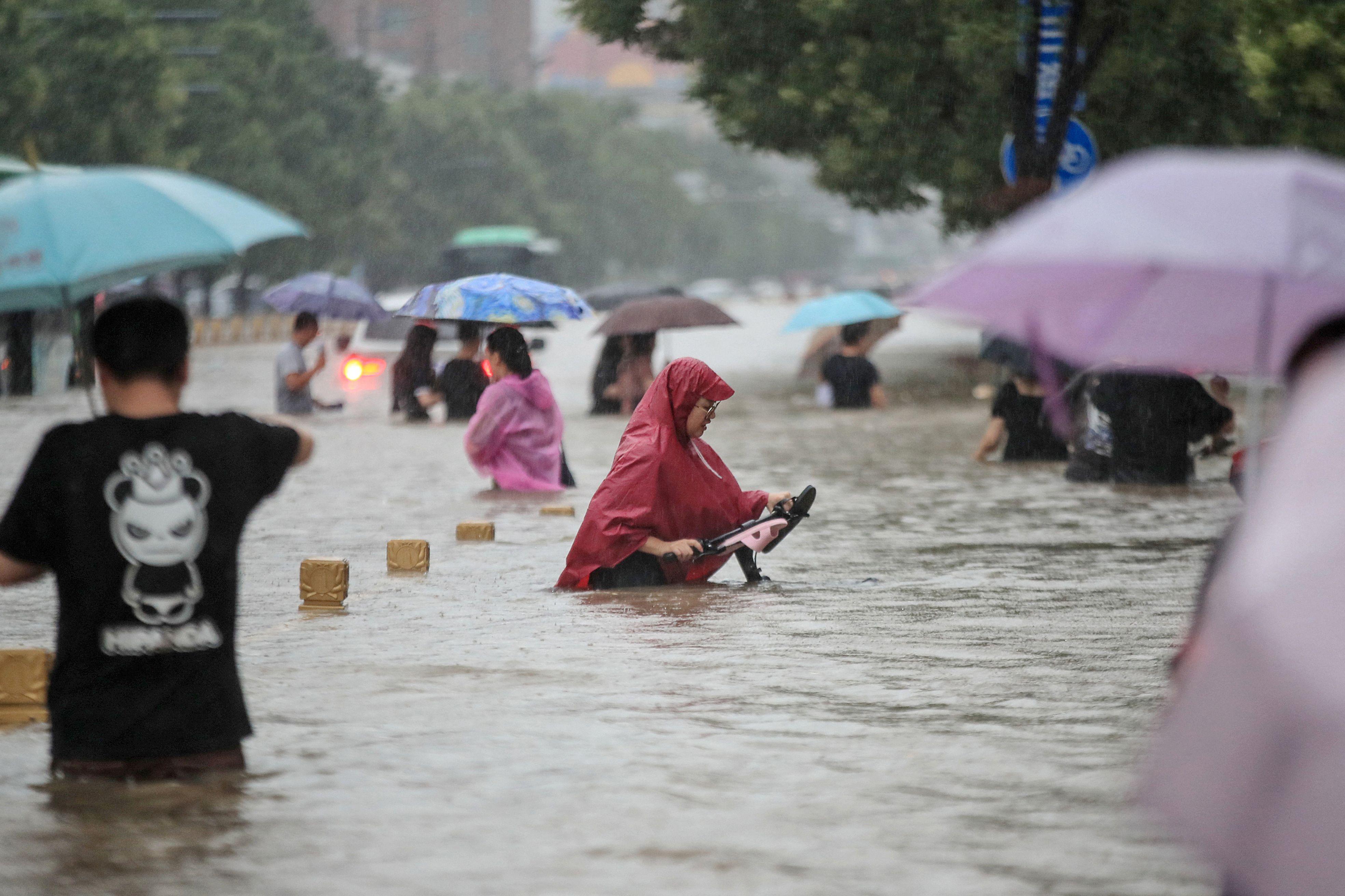 This photo taken on July 20, 2021 shows people wading through flood waters along a street following heavy rains in Zhengzhou in China's central Henan province. 