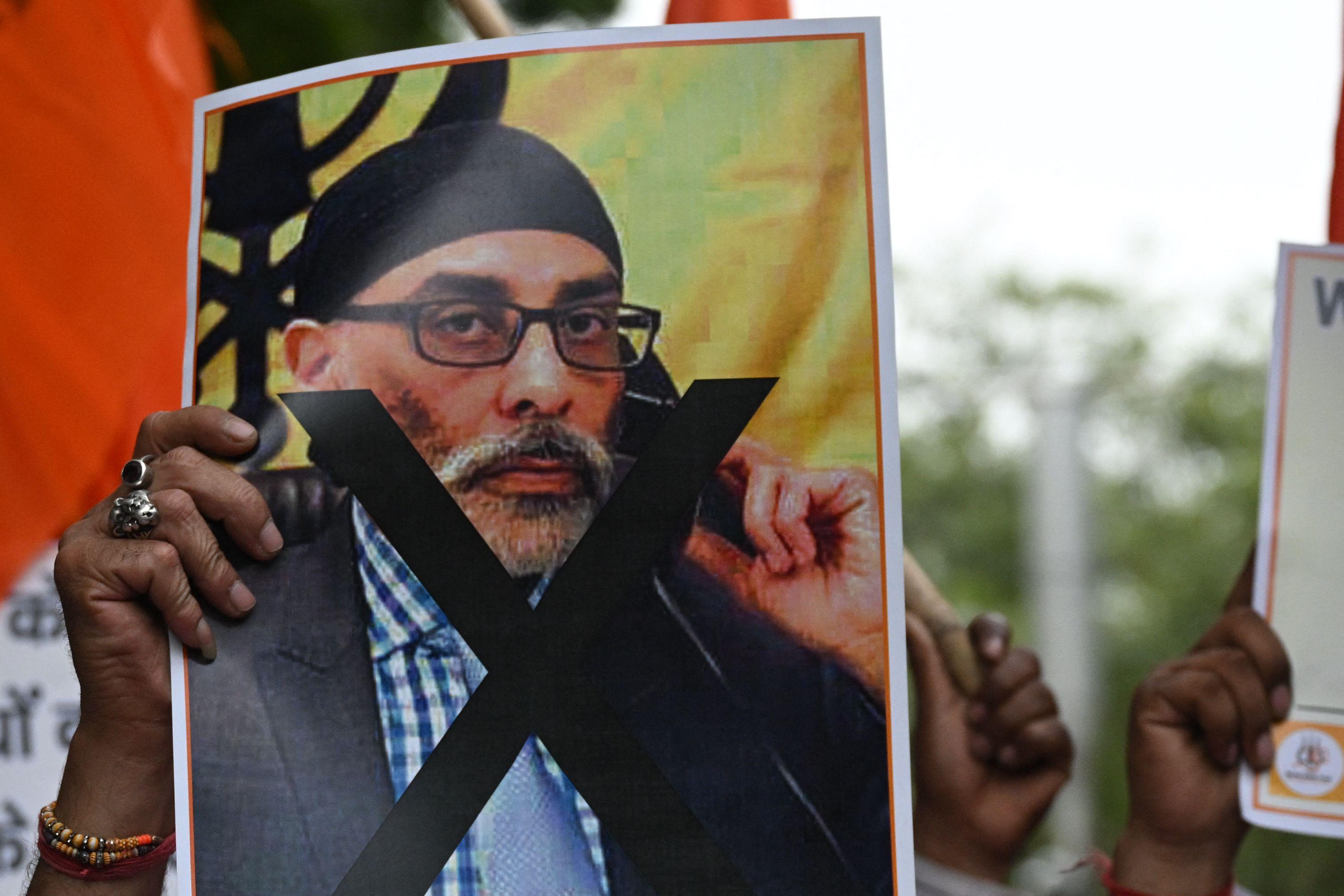 A protester holds up a photo of Gurpatwant Singh Pannun with an X imposed over his body.