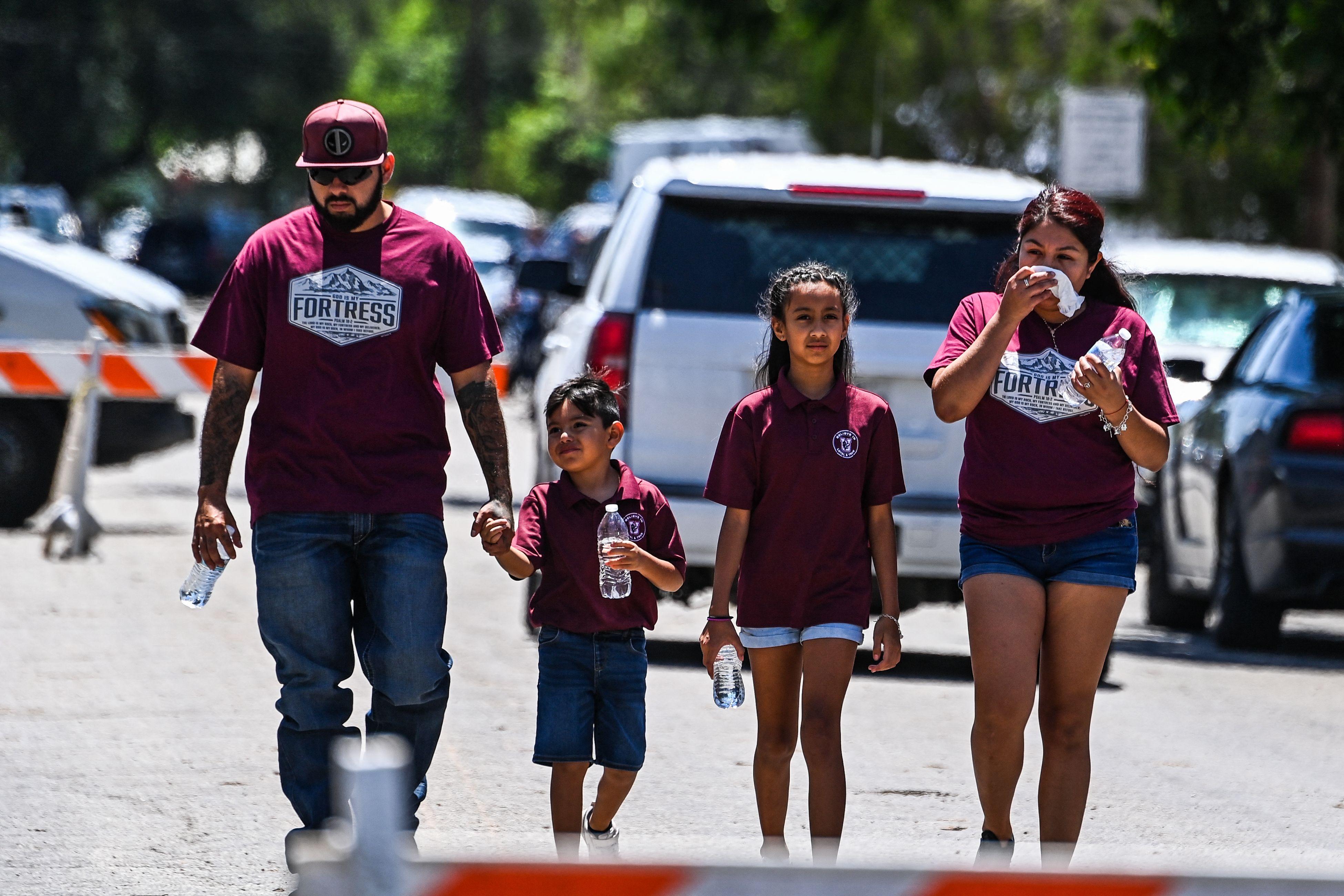 A man holds a young boy's hand, walking next to a girl and a woman who appears to be wiping her face with a tissue. 