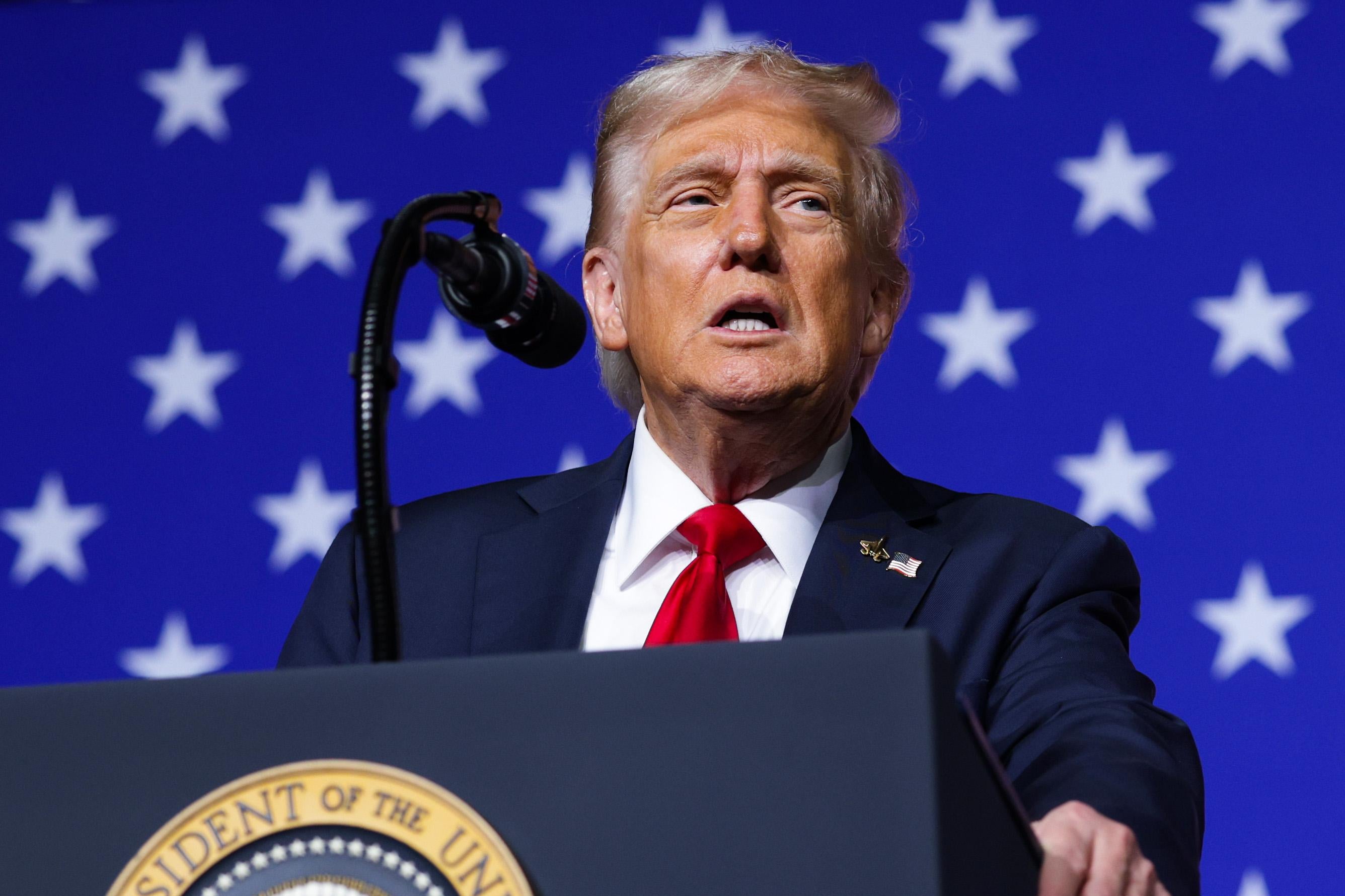 Präsident Trump wendet sich an den General, hinter ihm eine amerikanische Flagge und vor ihm ein Präsidentensiegel.
