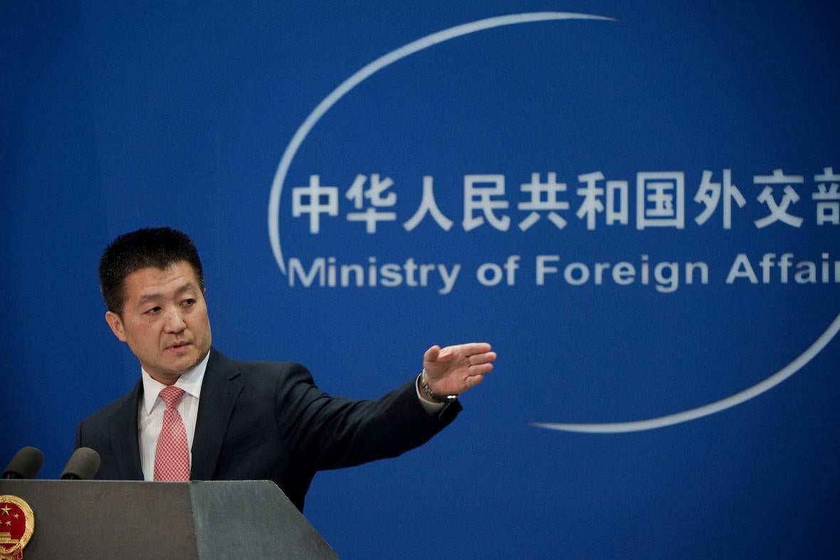 Lu Kang points from a lectern, in front of a backdrop that reads "Ministry of Foreign Affairs."