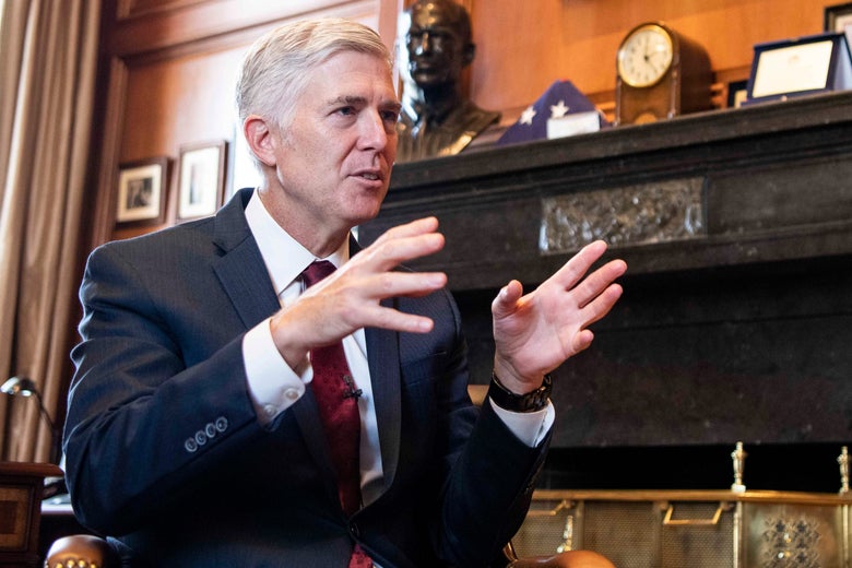 Neil Gorsuch, seated in front of a fireplace, talking with his hands held up.