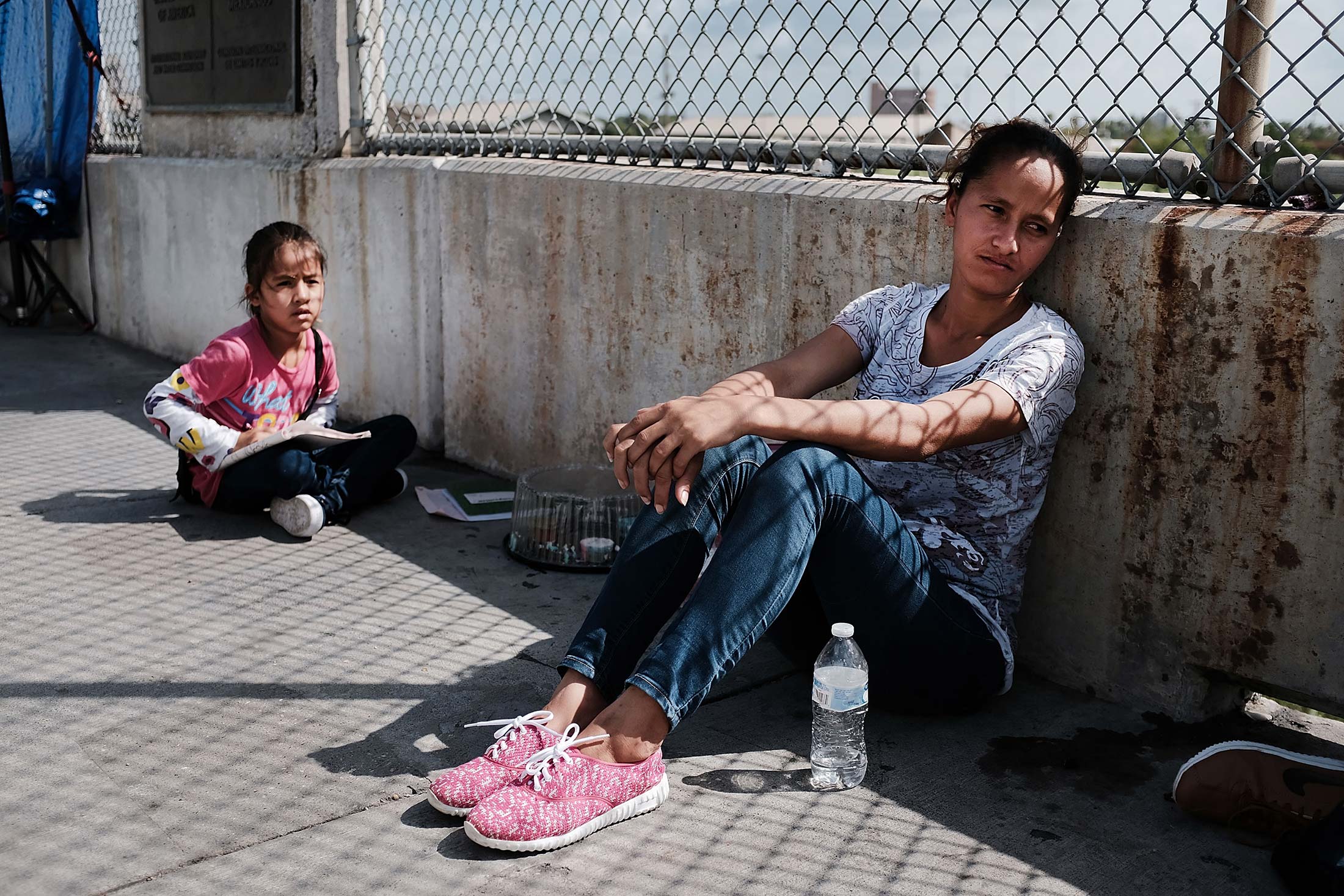 Migrant woman and child sitting on concrete bridge.