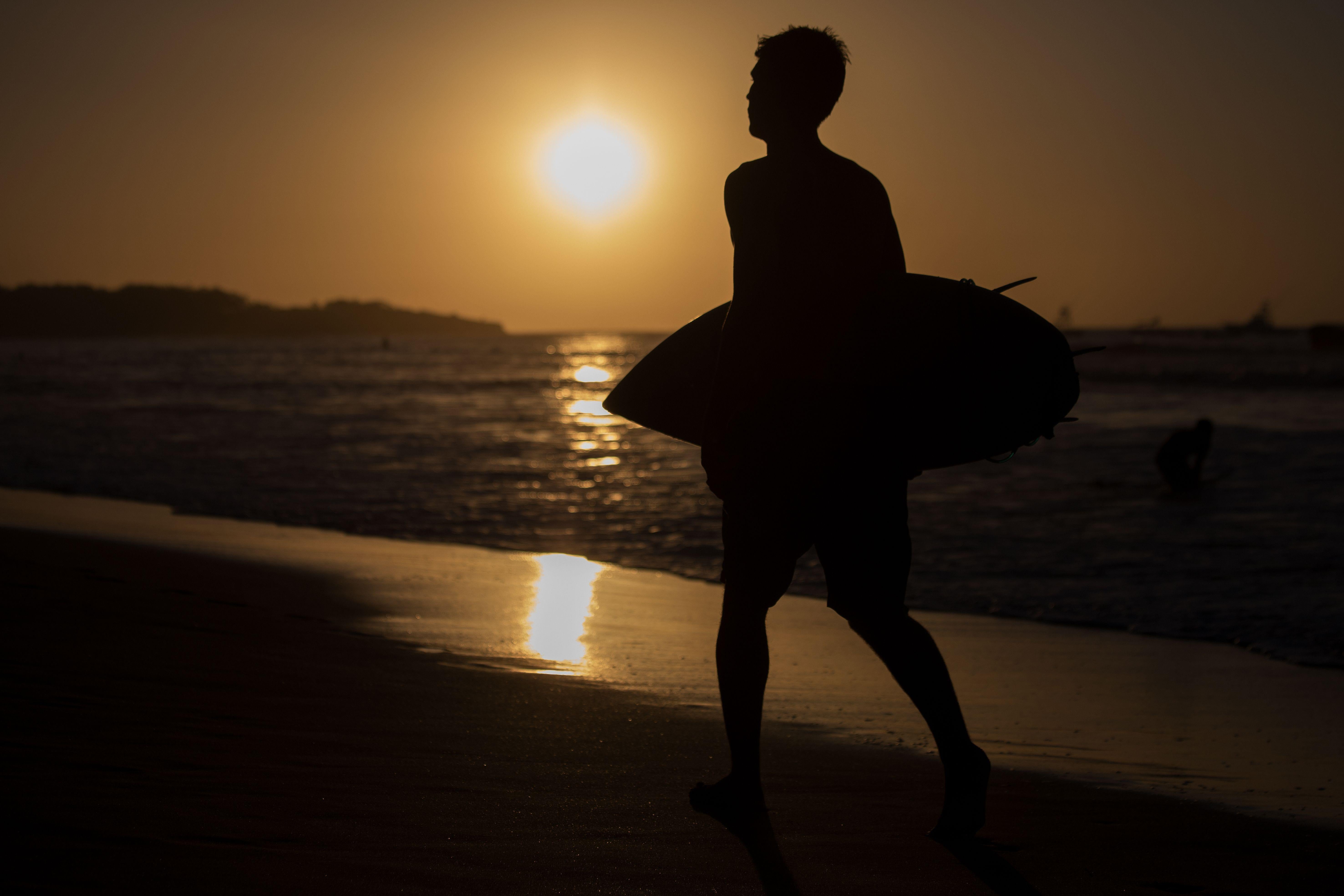 A man carries a surfboard as he walks past the setting sun at the beach in Tamarindo, Costa Rica on December 12, 2018. 