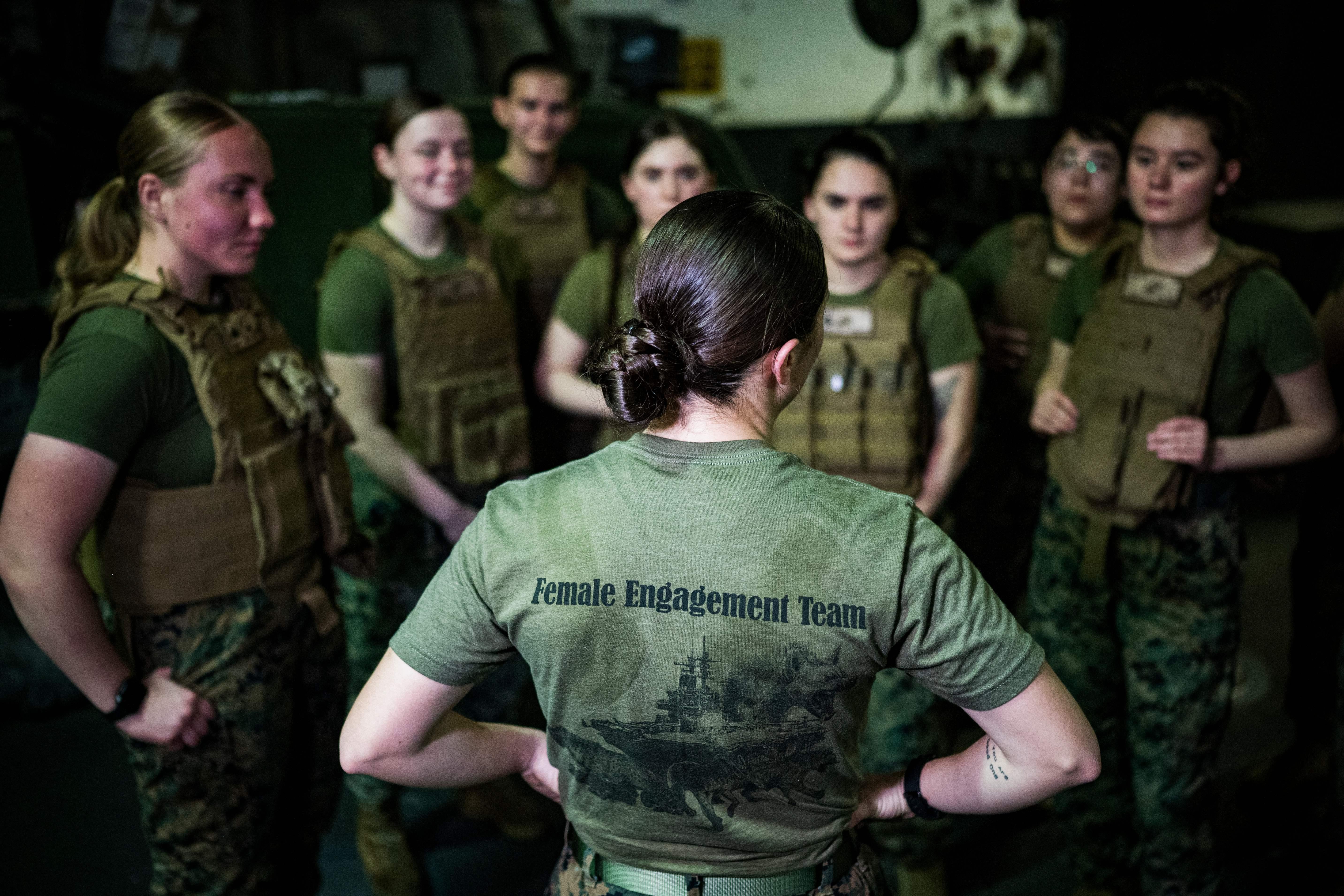 Female Marines stand in a group listening to a leader.