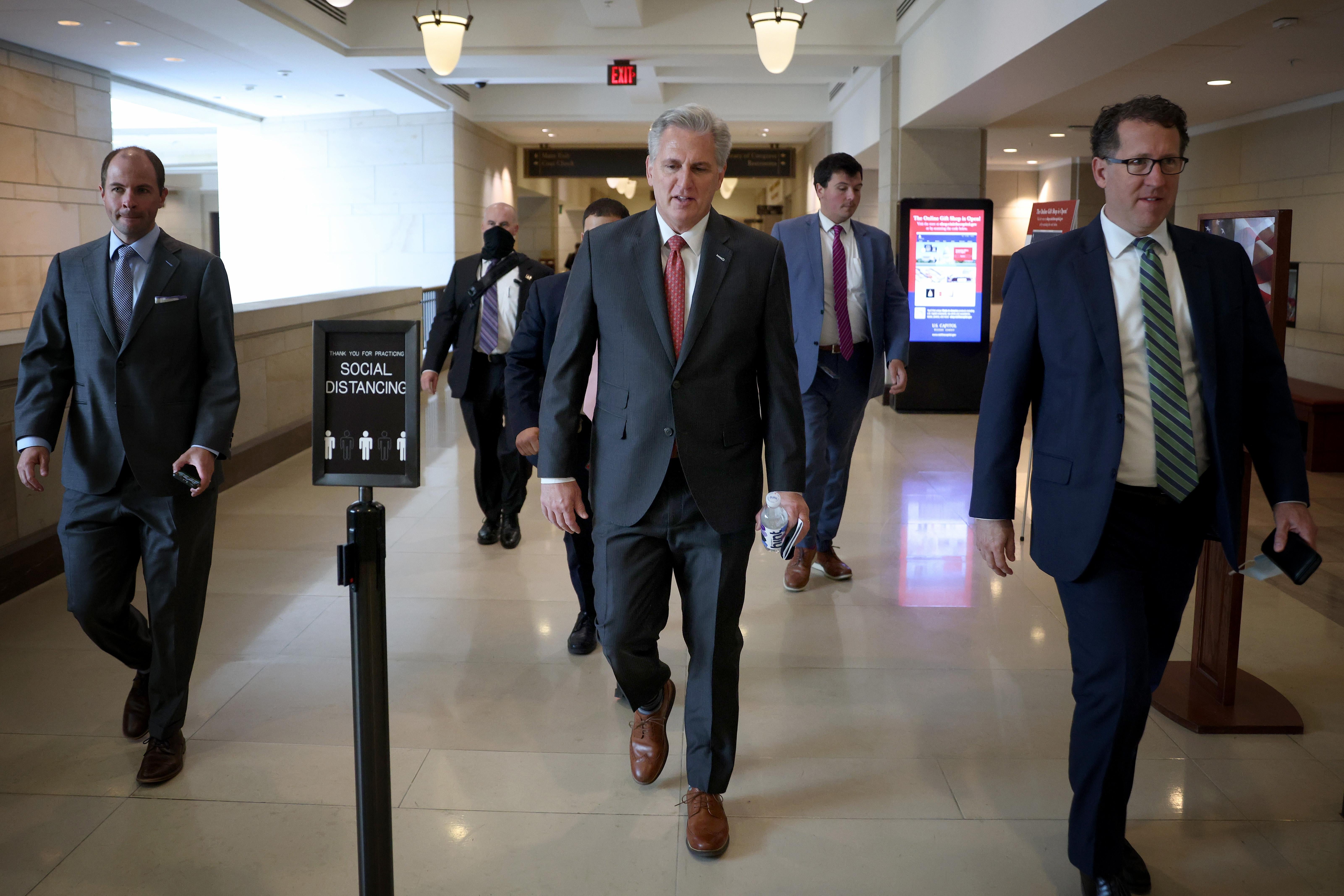 Kevin McCarthy leaves a meeting of the House Republican Conference, walking down a hallway with several men in suits around him