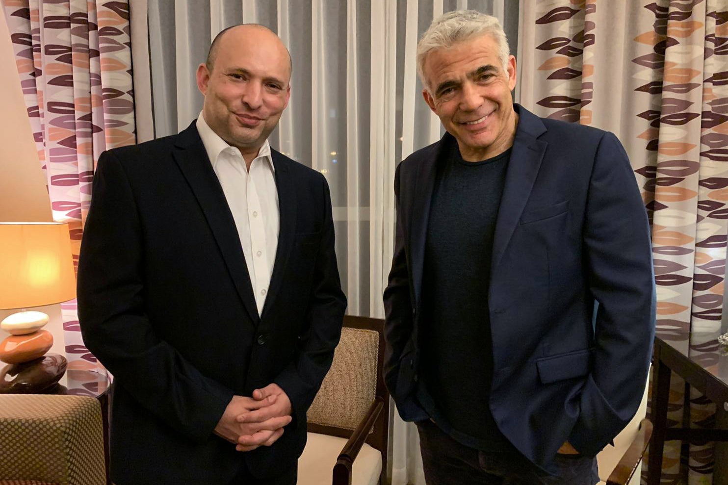 Bennett and Lapid standing in front of patterned curtains, smiling.