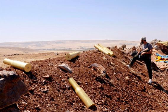A man belonging to forces loyal to Syria's President Bashar al-Assad stands next to spent ammunition rounds in Tal El-Tineh village, during what they said was an operation to occupy it,  in the southern countryside of Aleppo, June 16, 2013.