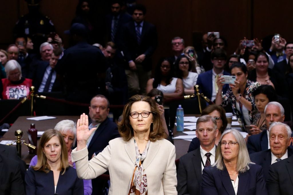 Gina Haspel raises her right hand to be sworn in in front of a crowded hearing room.