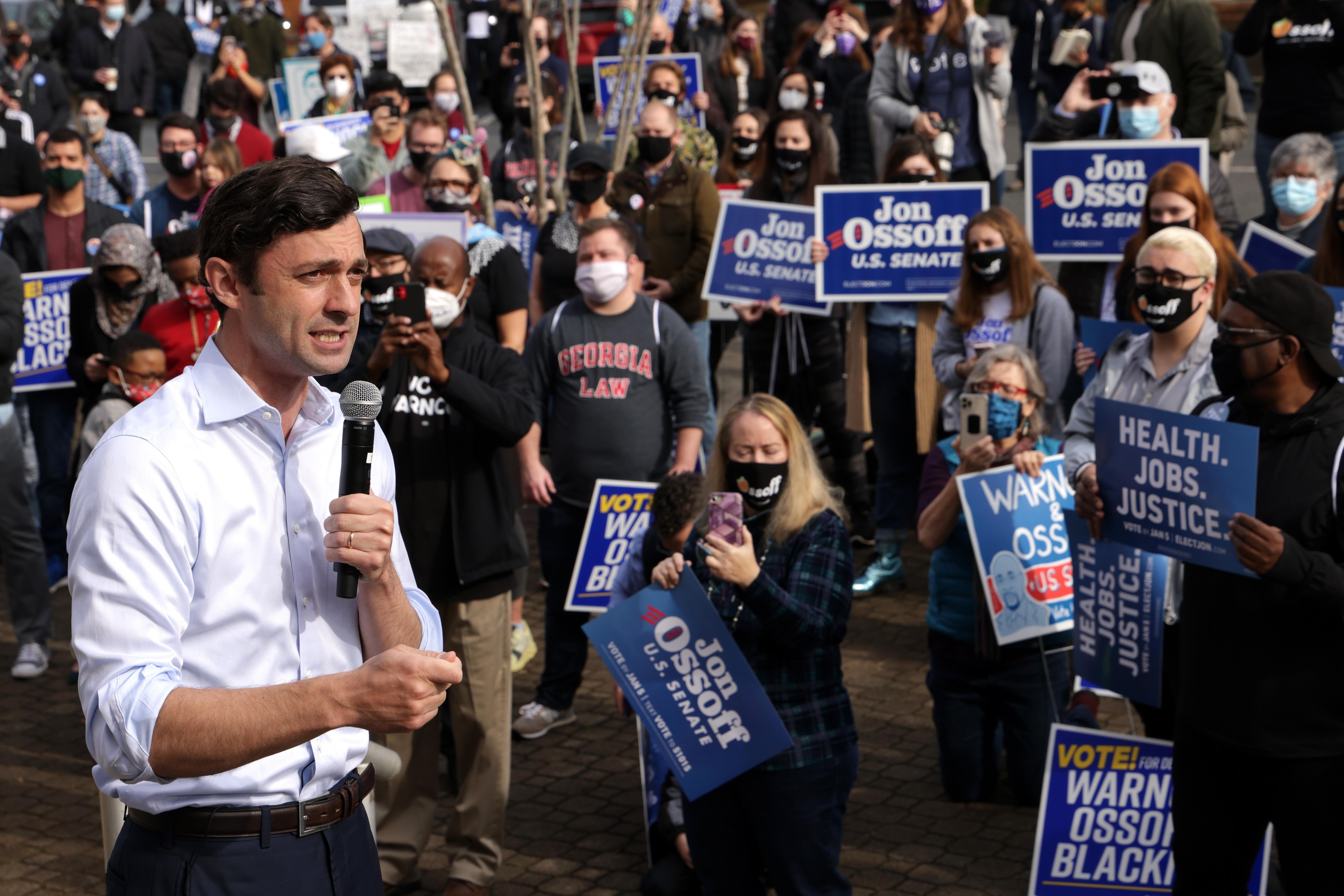 Jon Ossoff speaks to a crowd holding Ossoff and Warnock signs.