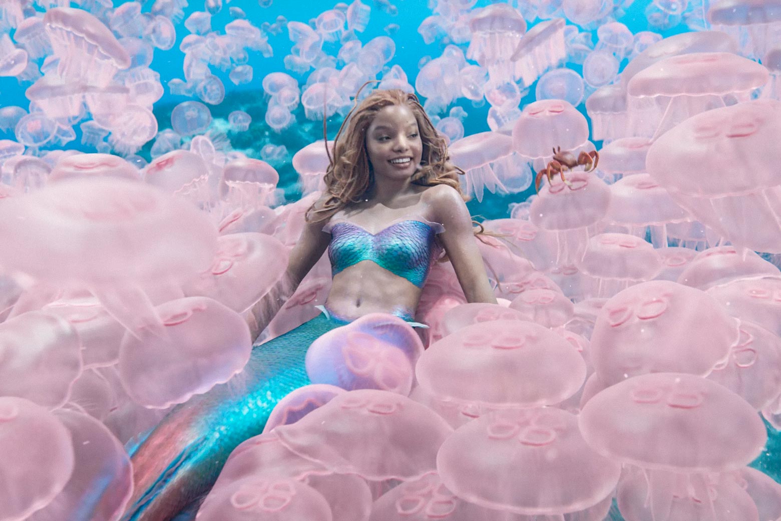 Ariel sits on a large group of bright pink jellyfishes and smiles.