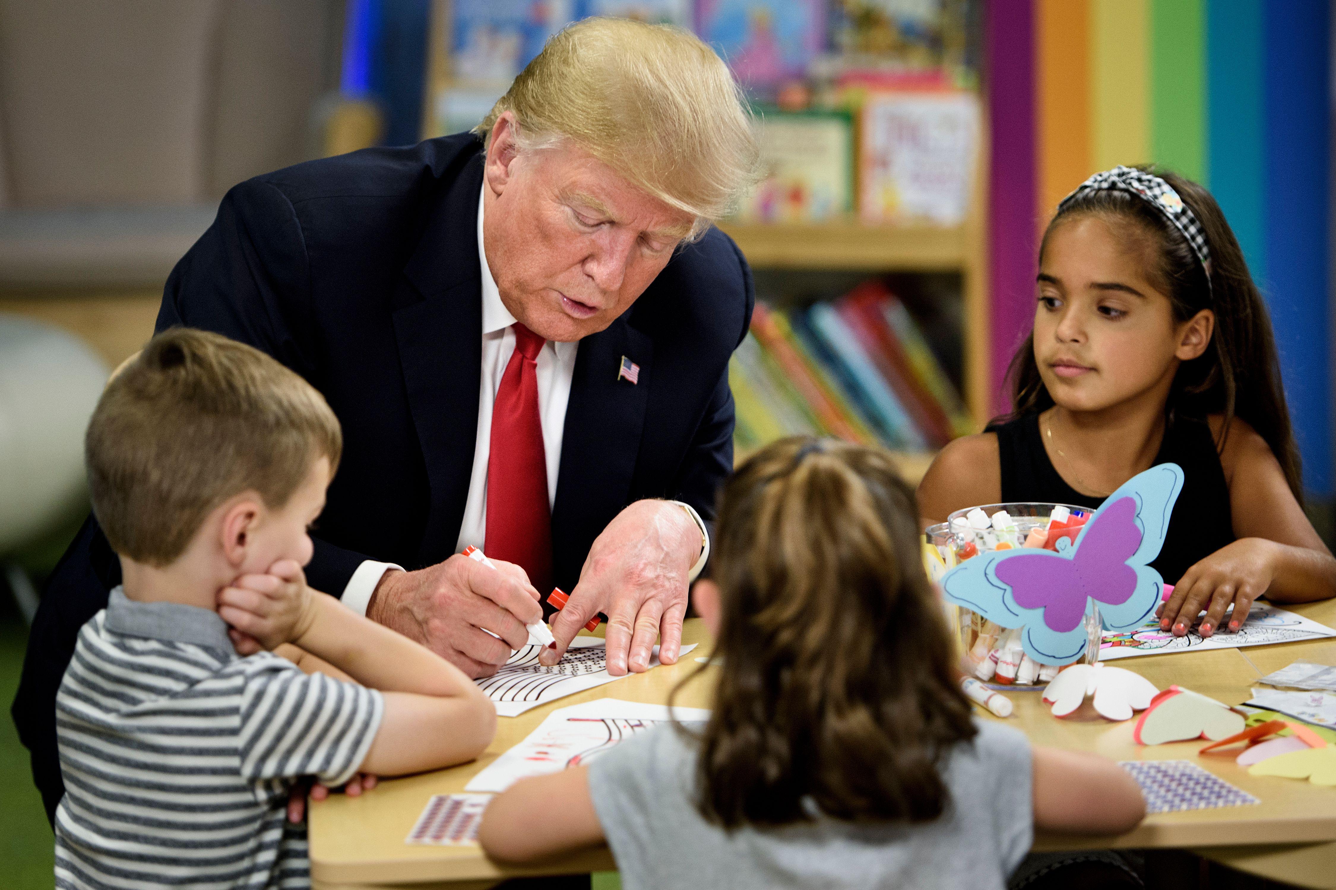 President Donald Trump colors in an American flag while children seated around him look on and color.